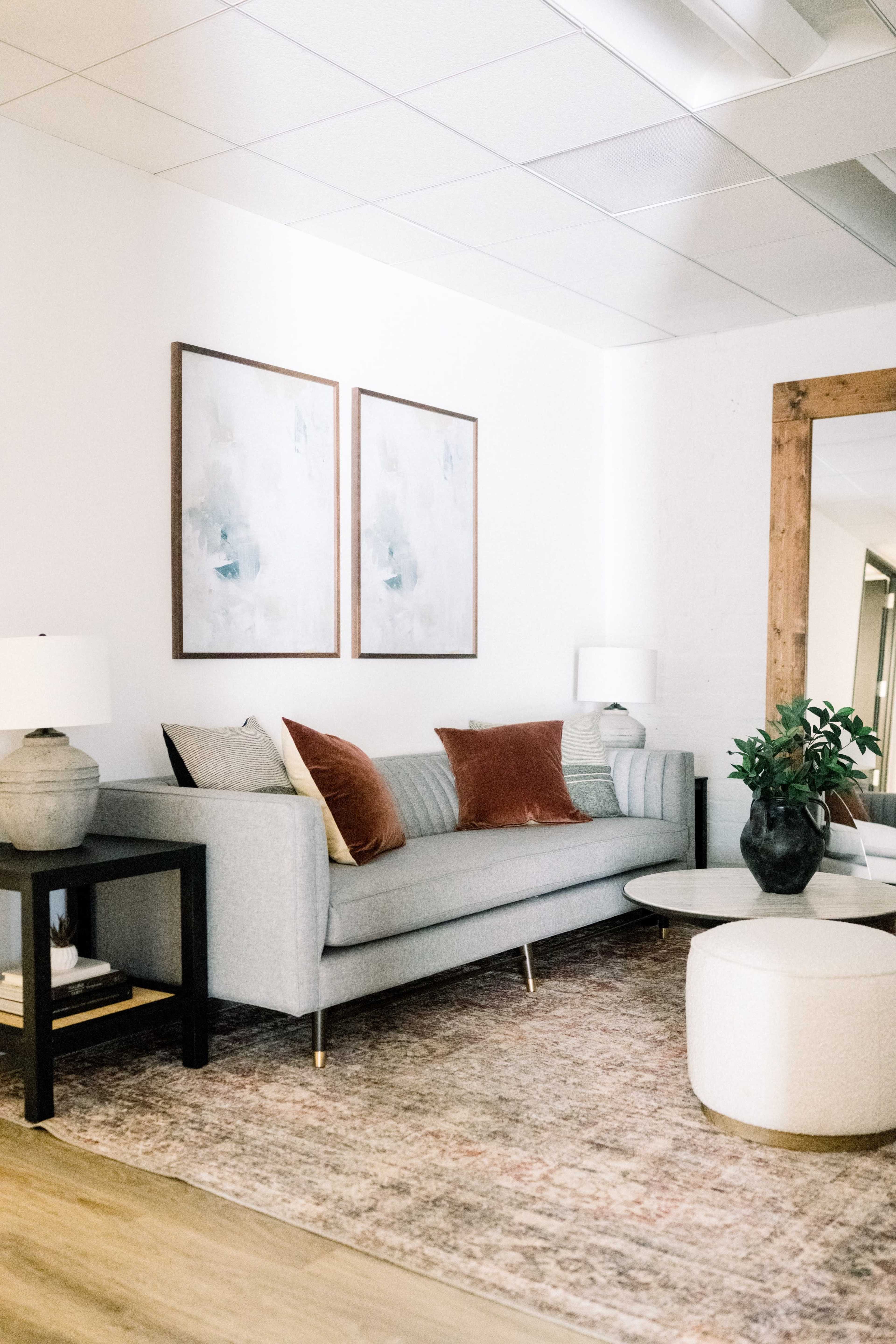 A modern living room with a gray sofa, two decorative pillows, a round coffee table, a potted plant, and framed artwork on the walls.