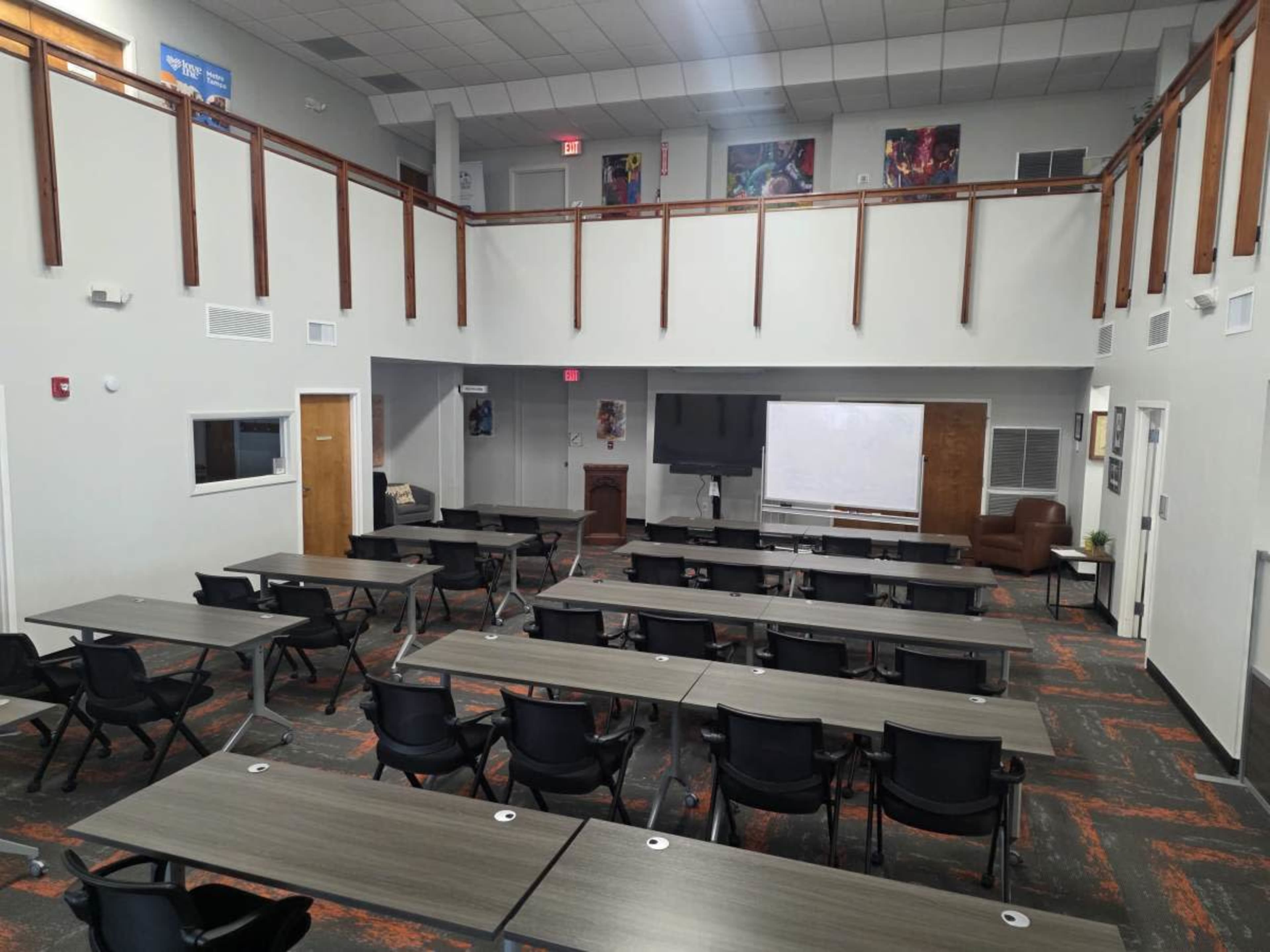 The image shows a spacious conference room with rows of tables and chairs, a large screen, and a podium at the front.