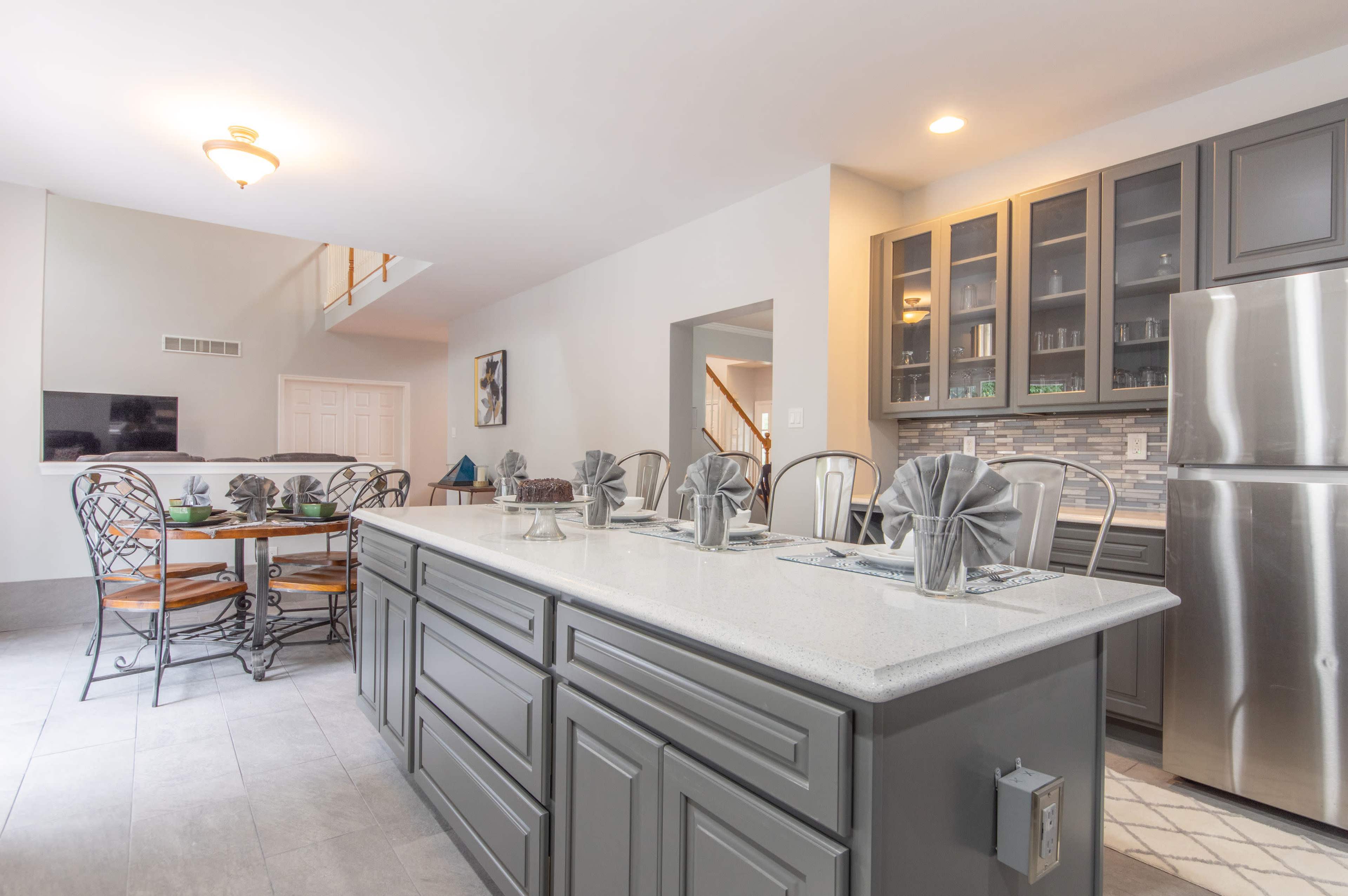 A modern kitchen with a large island, steel appliances, gray cabinetry, and a dining area featuring a round table with metal chairs.