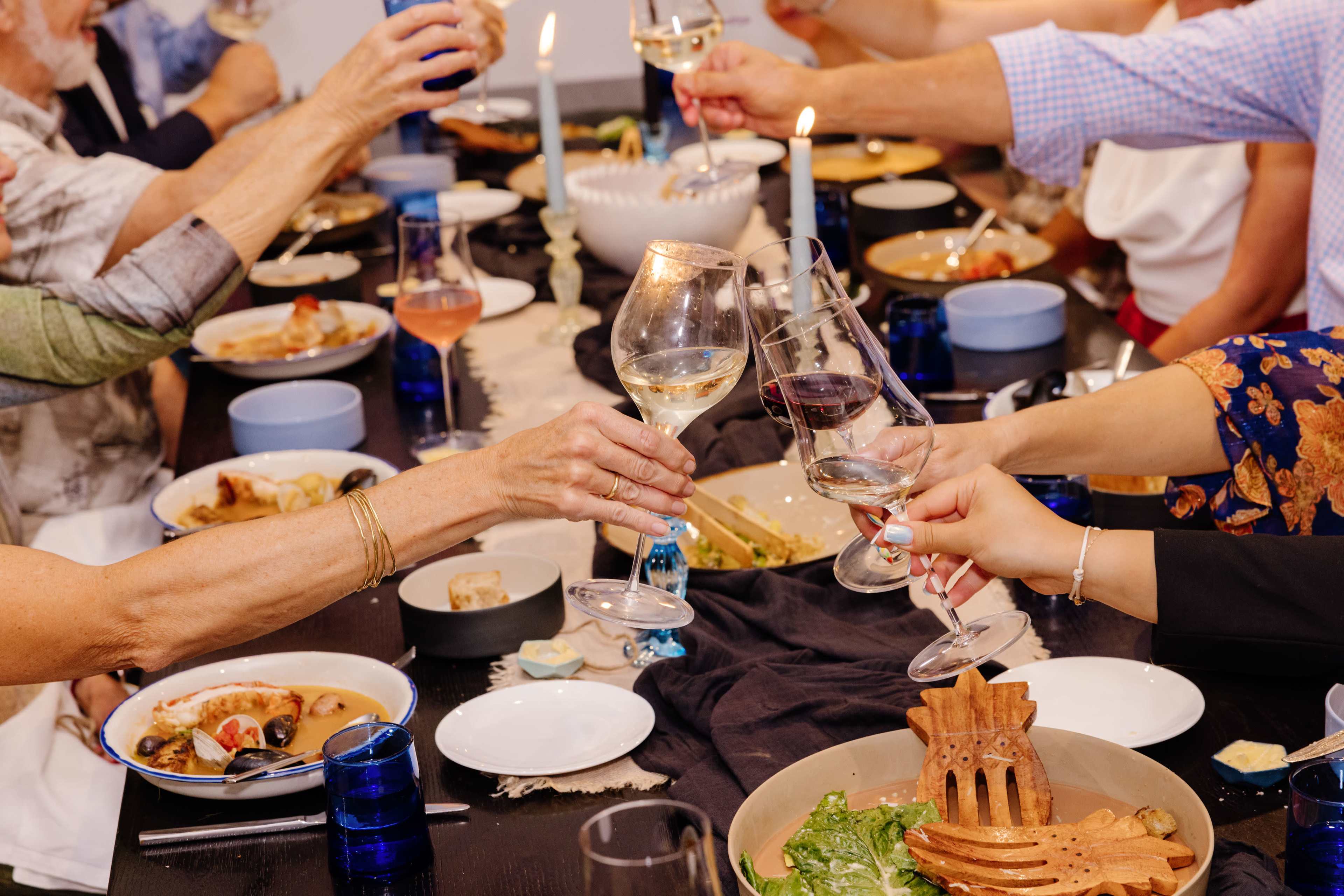 A group of people at a dining table raise their glasses in a toast while sharing a meal.