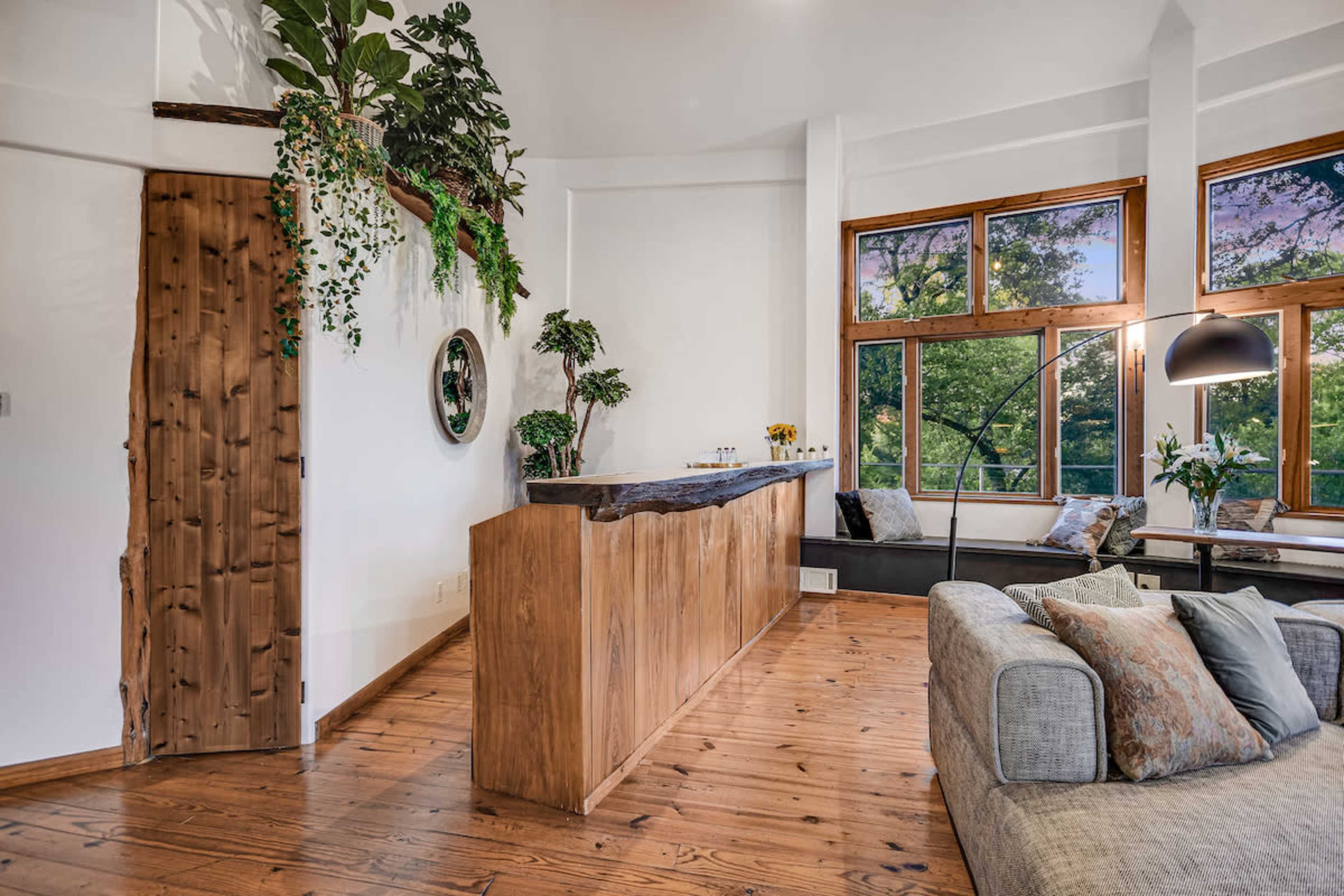 A modern living space with a wooden bar counter, large windows allowing natural light, and a cozy seating area with a sofa.
