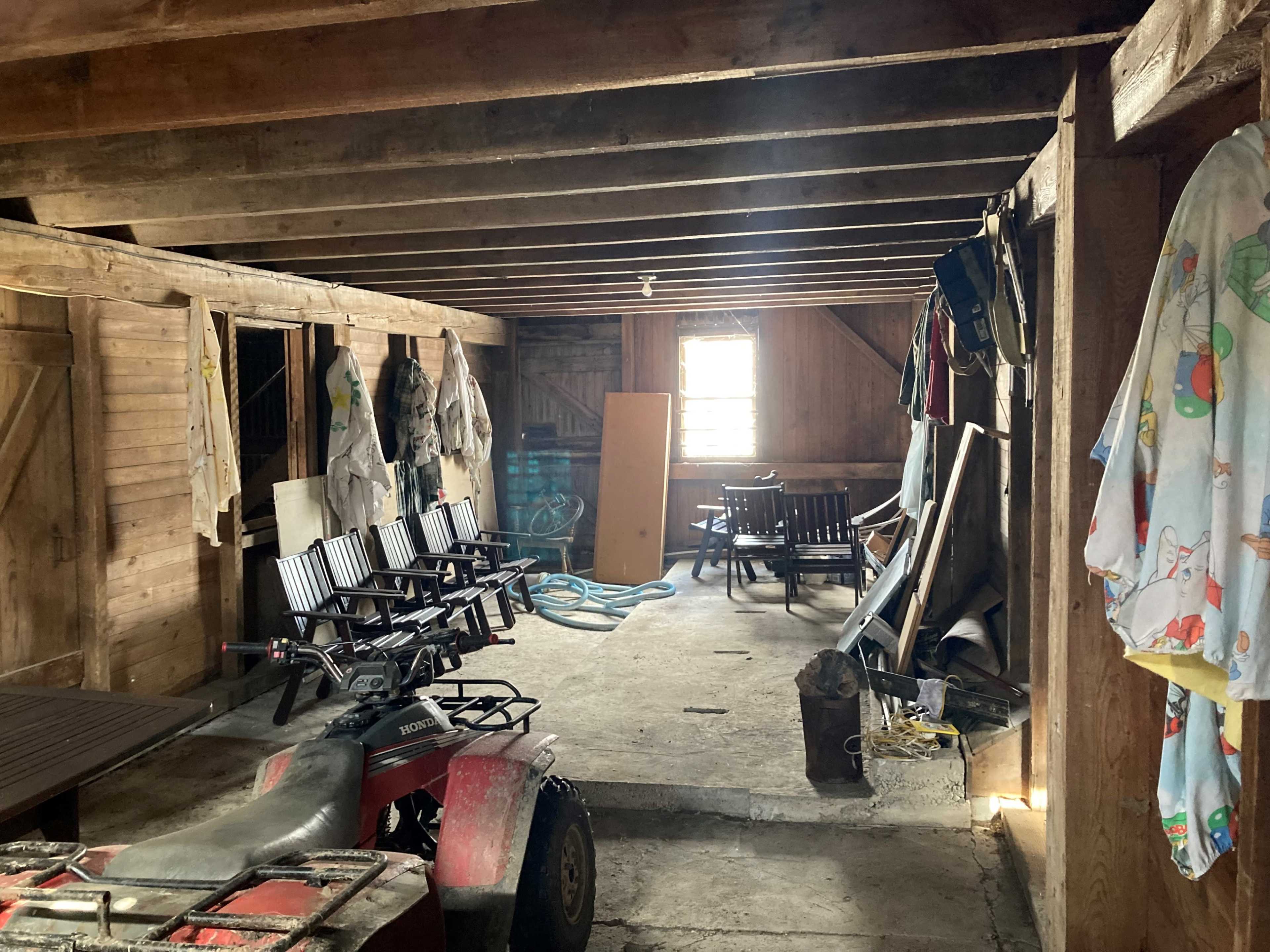 The interior of a wooden barn with various items, including chairs, a table, and an ATV, arranged along the walls.