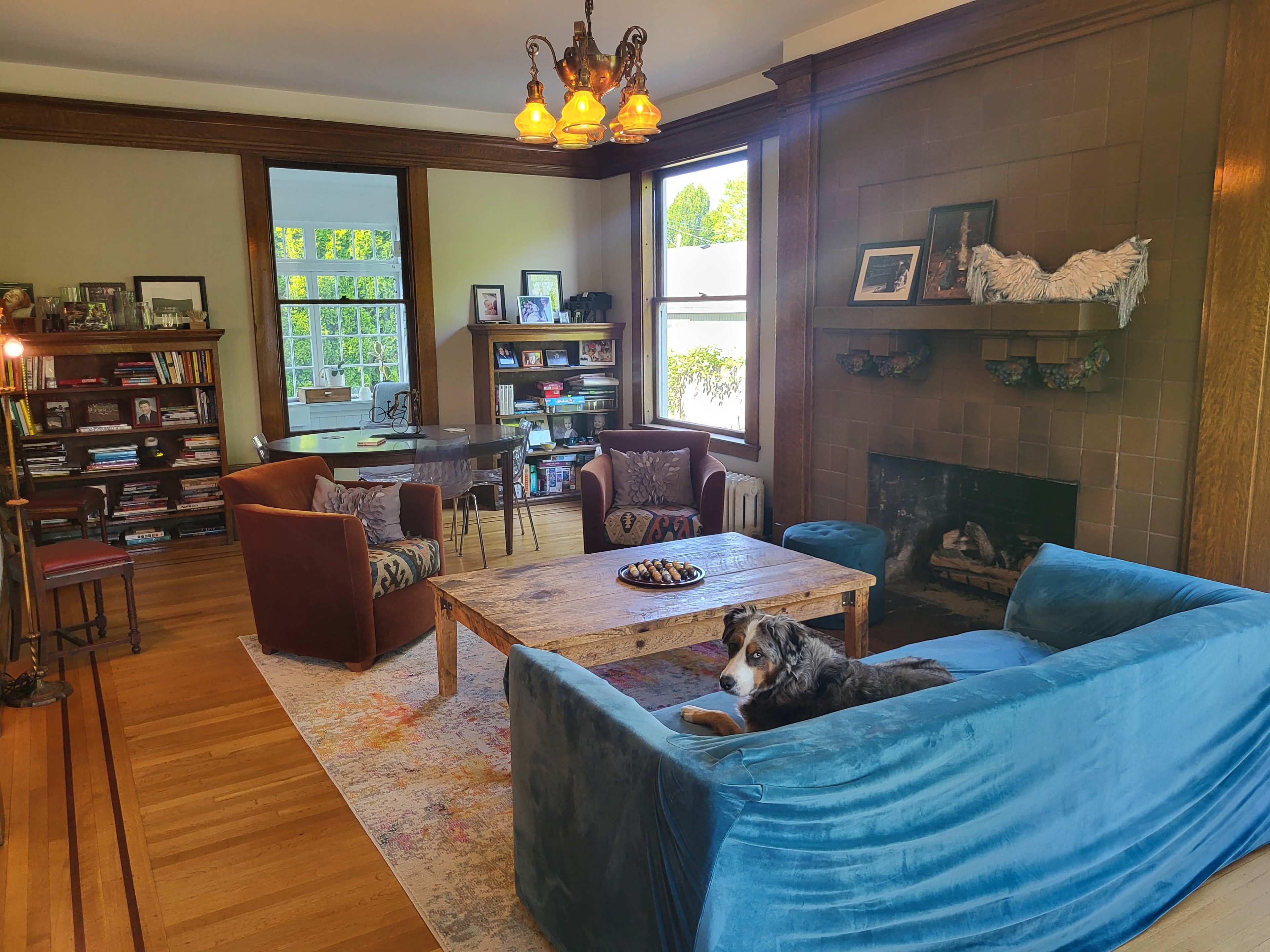 The image shows a cozy living room with a blue sofa, a wooden coffee table, a fireplace, and shelves filled with books.