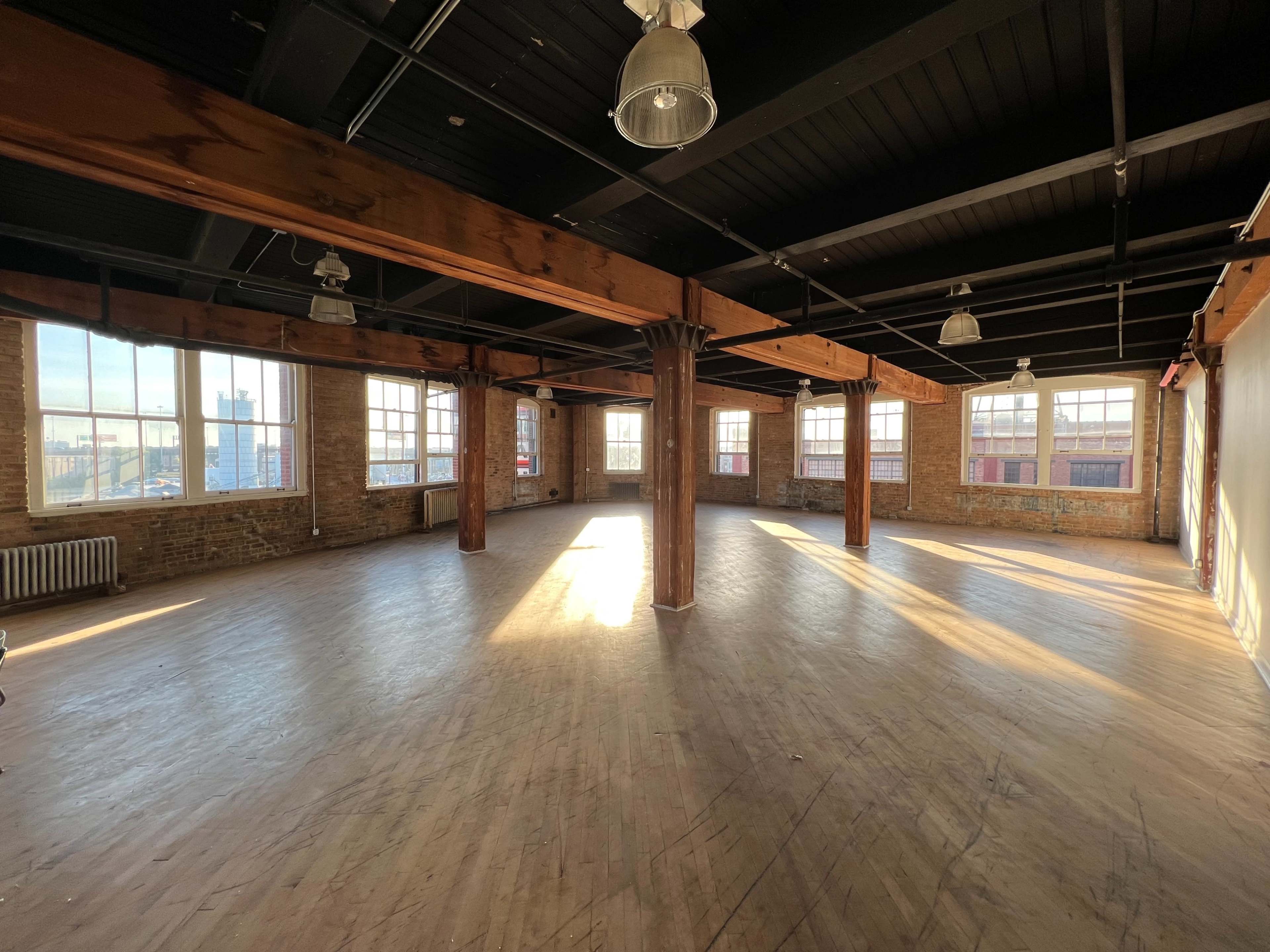 A spacious, brightly lit room with wooden floors, large windows, and exposed wooden beams.