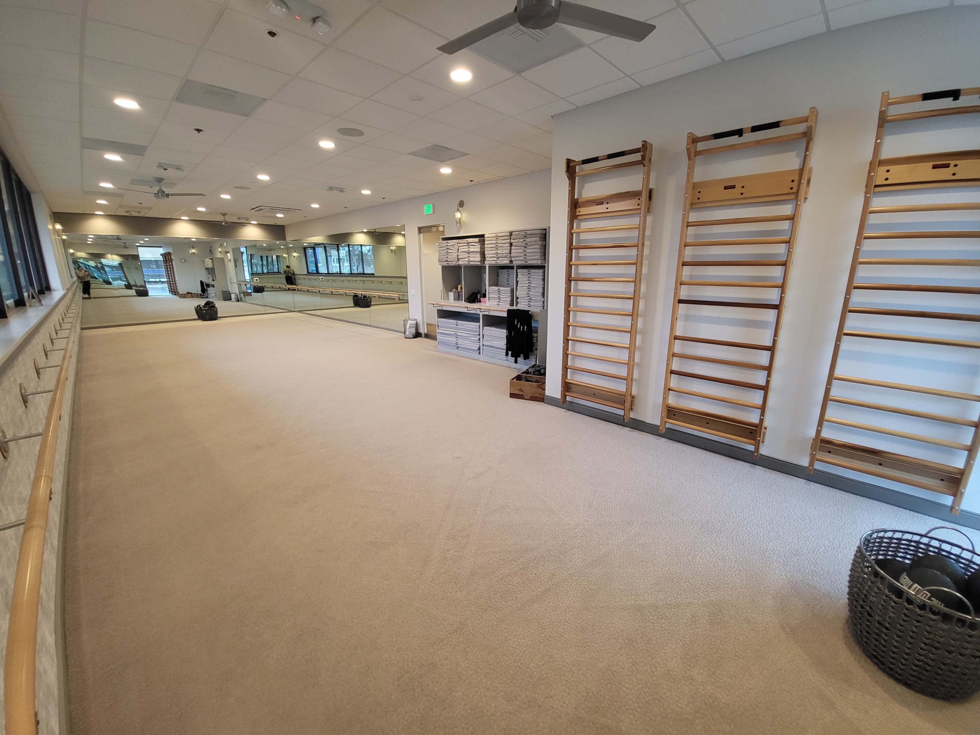 A spacious studio with wooden exercise bars, mirrors on the wall, and neatly arranged fitness equipment.