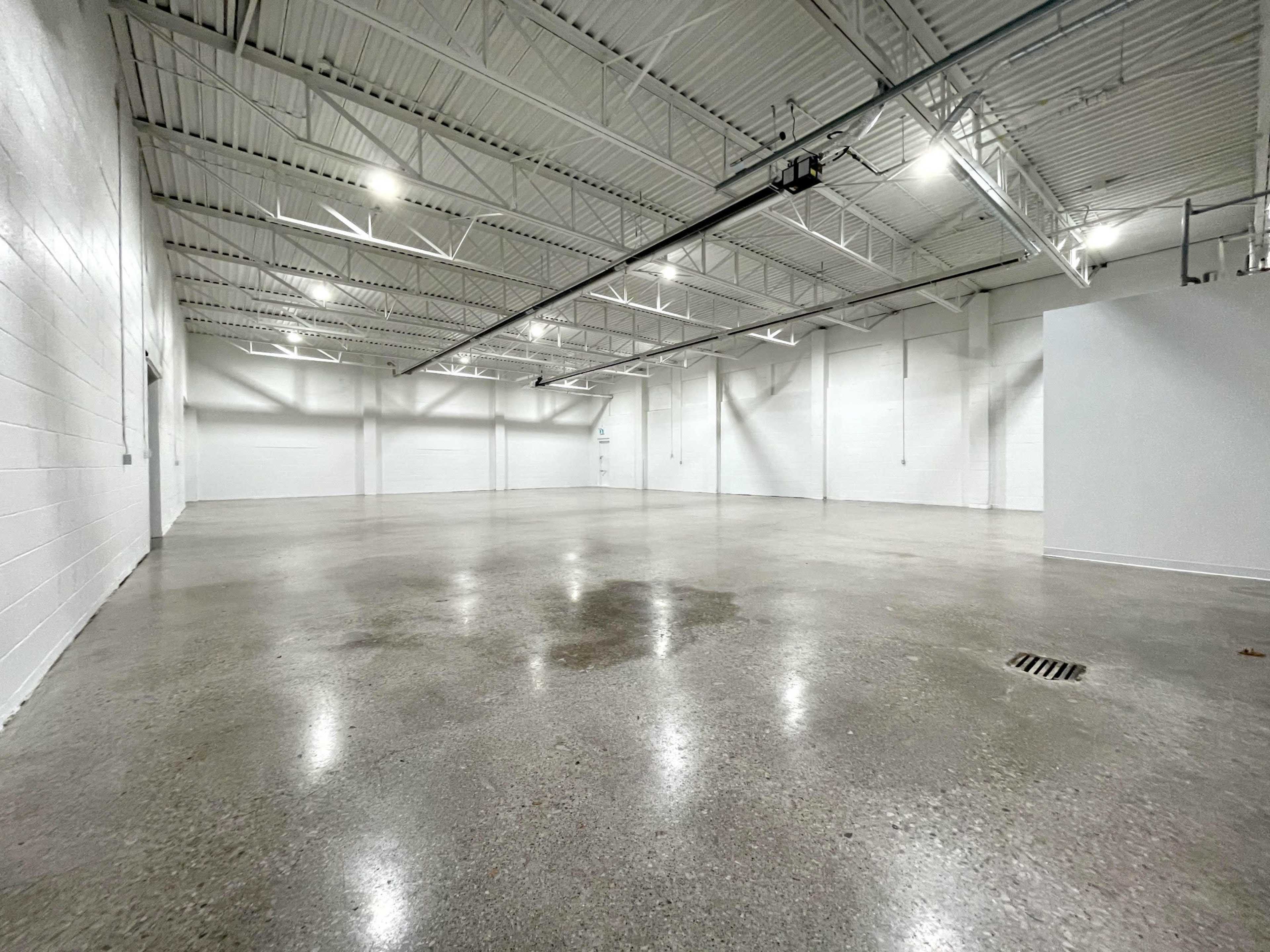 The image shows a large, empty warehouse space with polished concrete floors and bright overhead lighting.