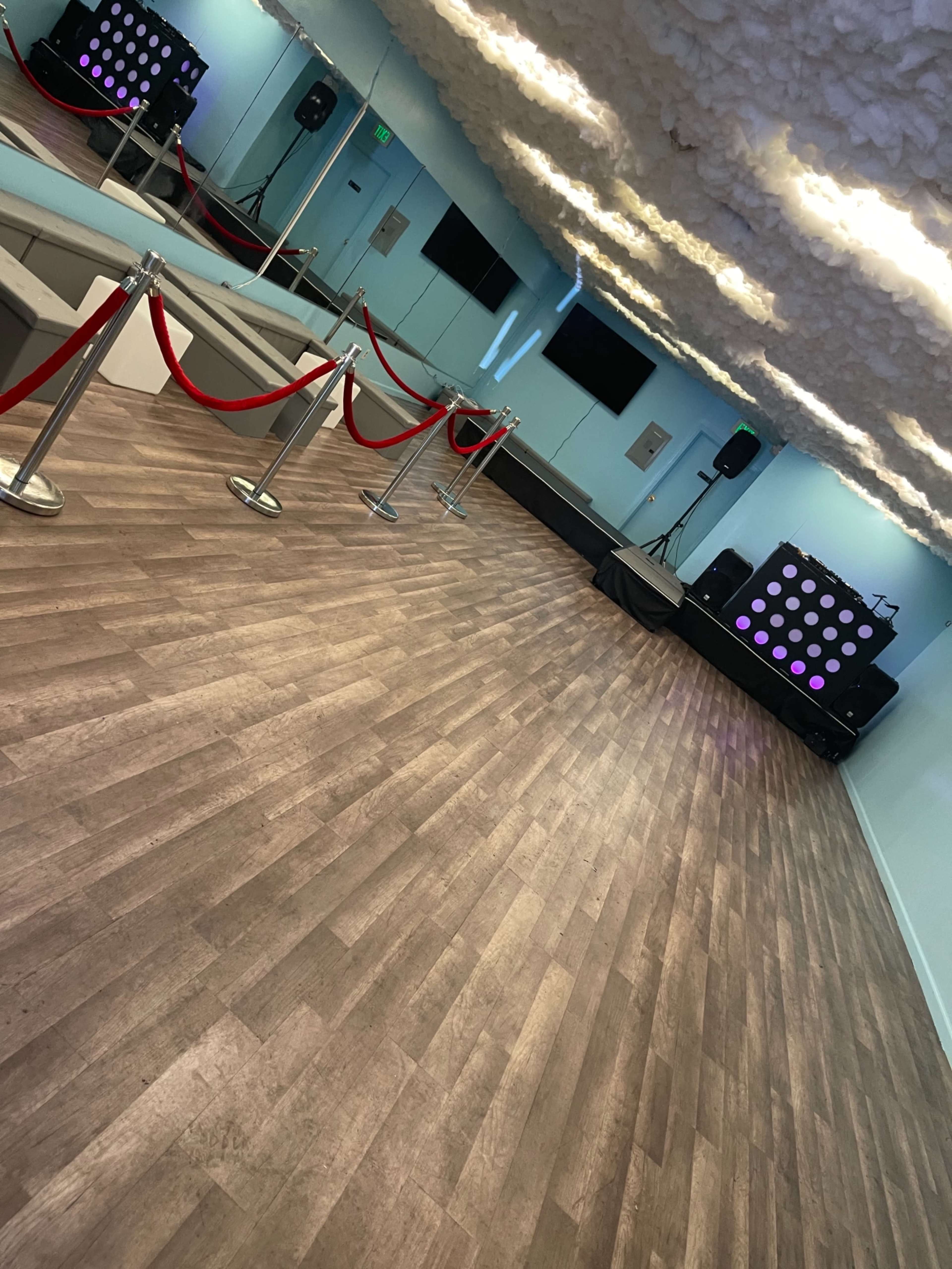 A spacious event room with wooden floors, a sound system, and red ropes creating a barrier.