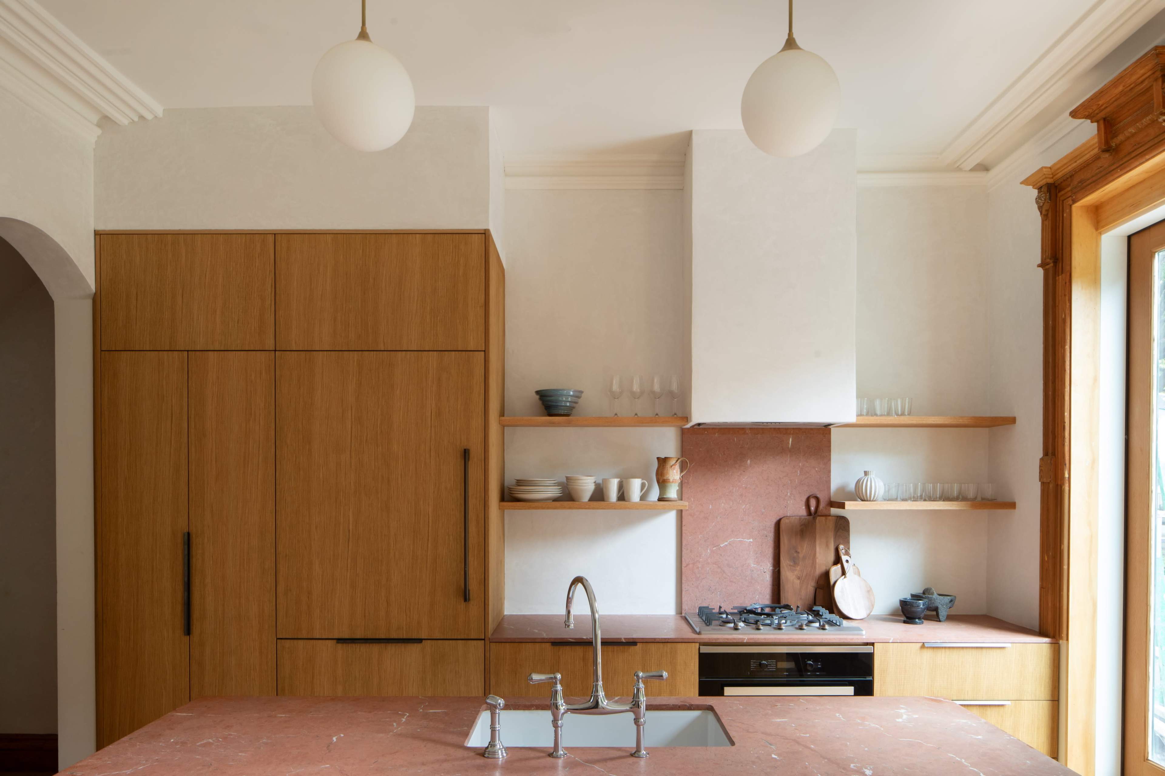 The kitchen features wooden cabinetry, a pink stone countertop, and open shelves displaying dishware.