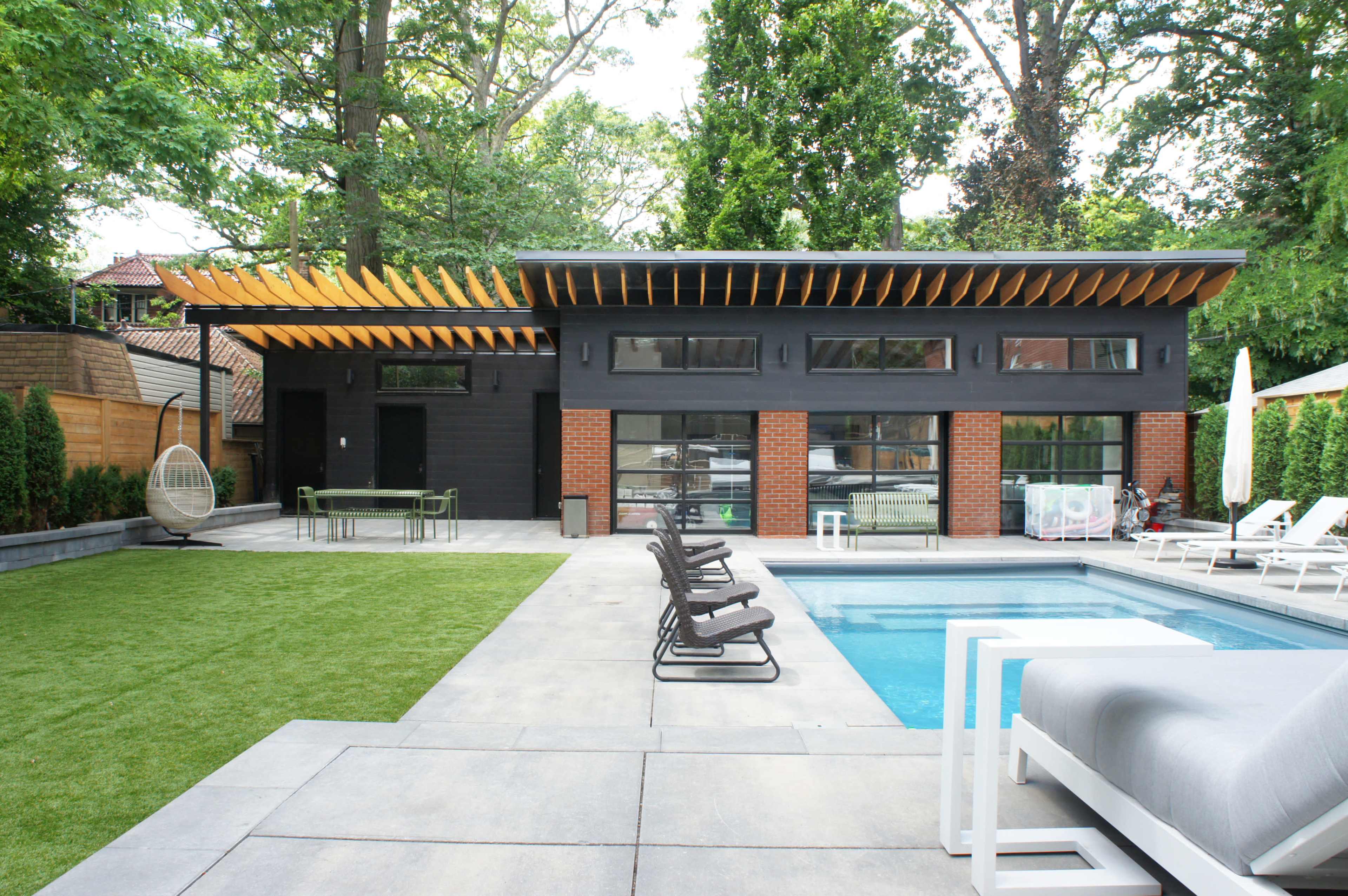 A modern house with large windows, a pool, and a well-maintained backyard featuring a lawn and patio area.