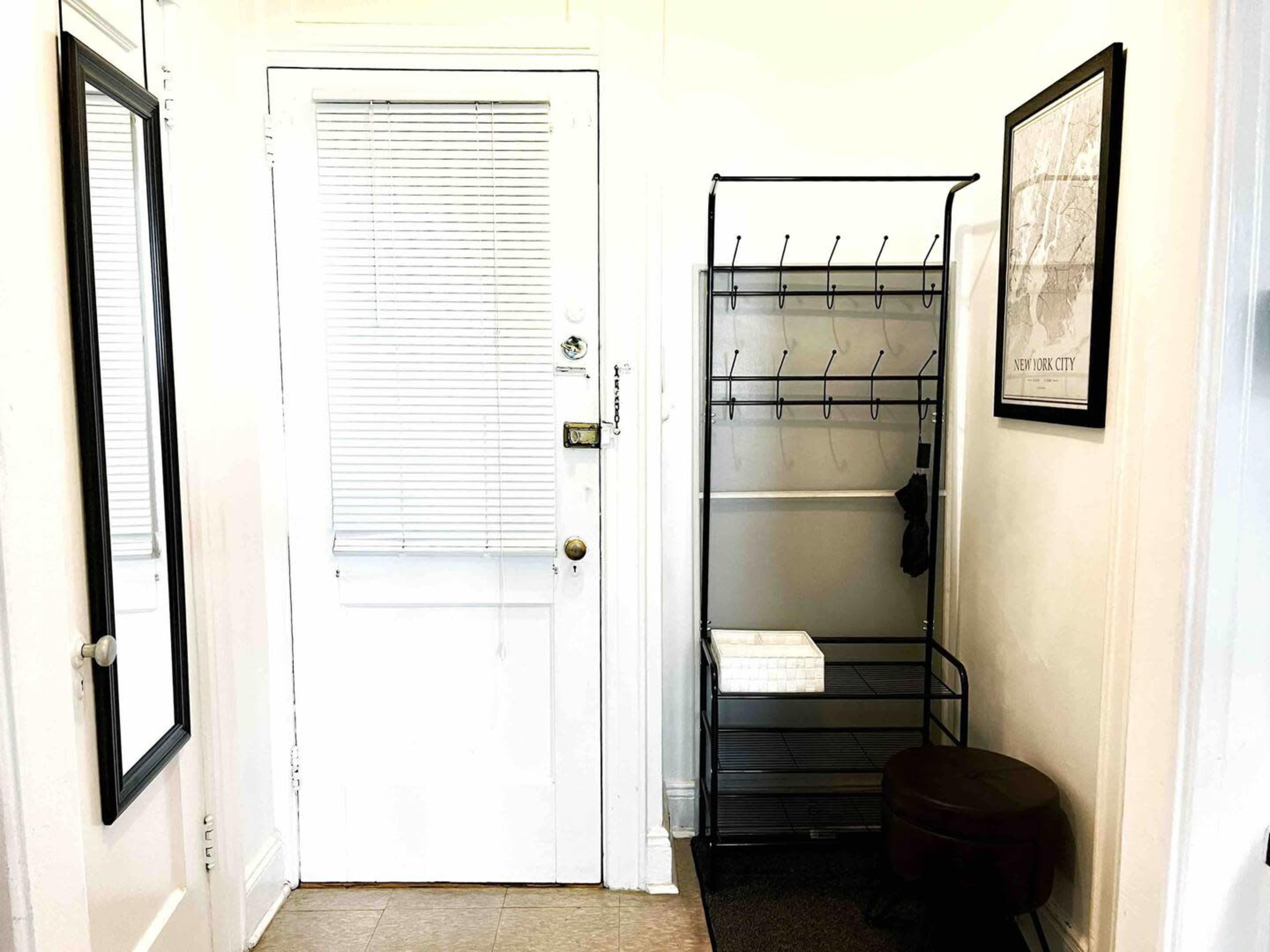 A small entryway with a door, a coat rack with multiple hooks, a bench, and a mirror on the wall.