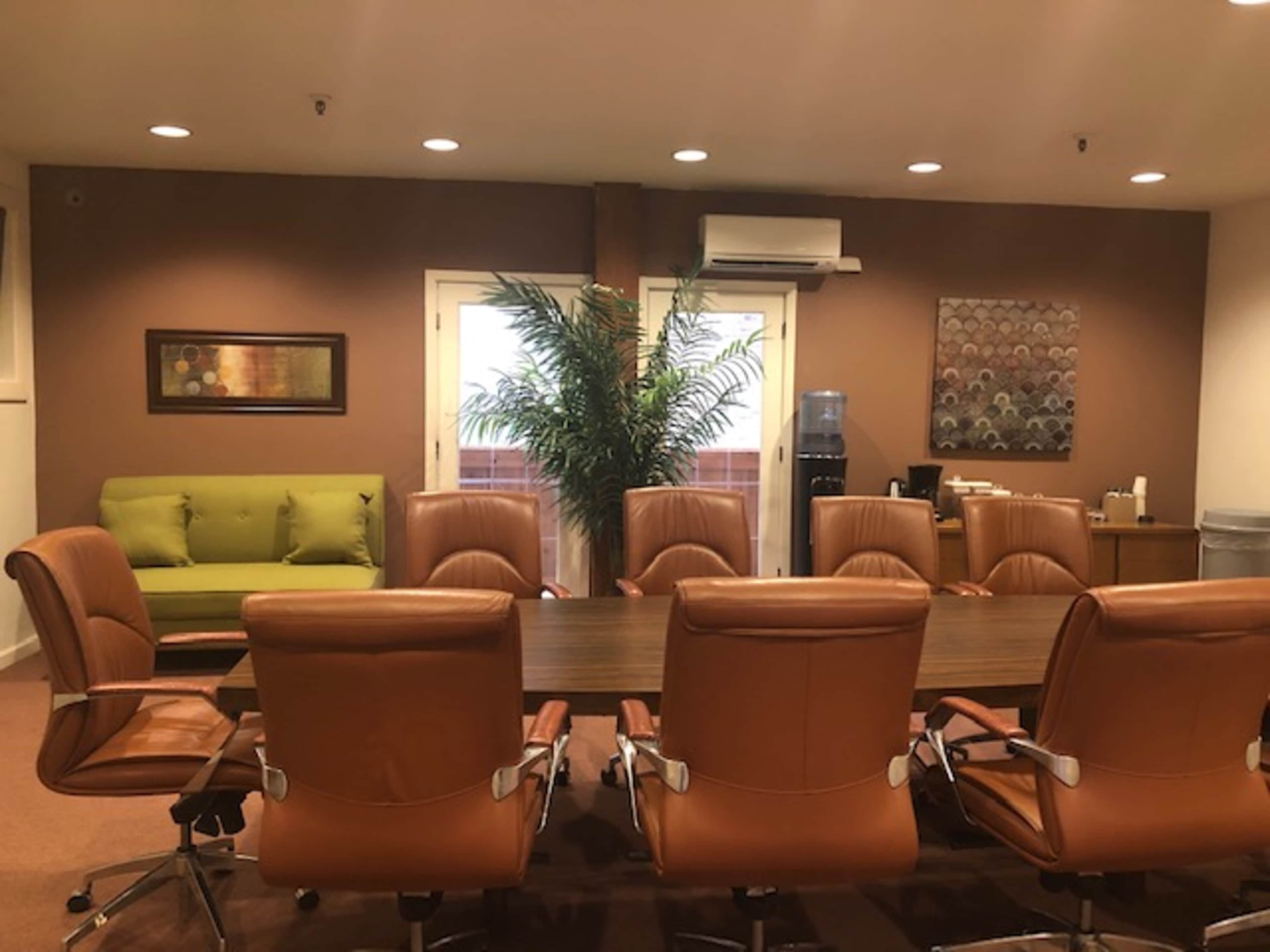 A conference room with a long wooden table surrounded by eight brown leather chairs and a green sofa against the wall.