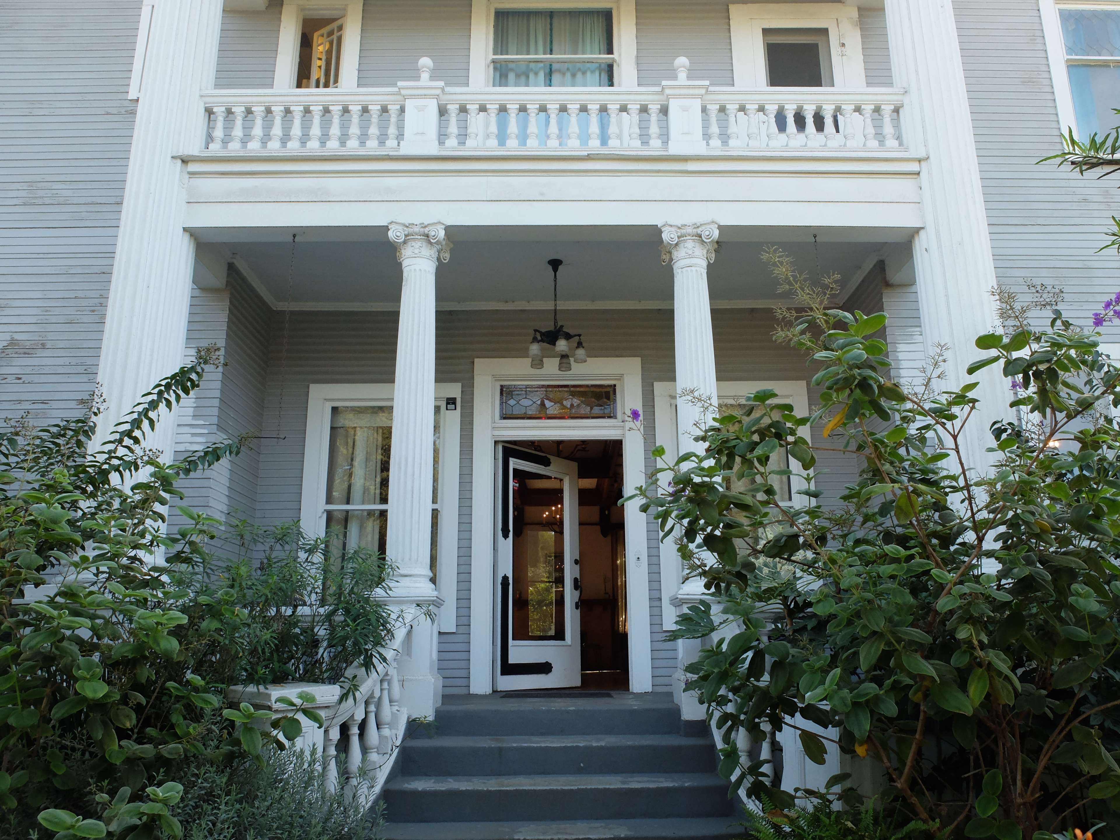 A two-story house with a front porch supported by columns, leading to an open door.
