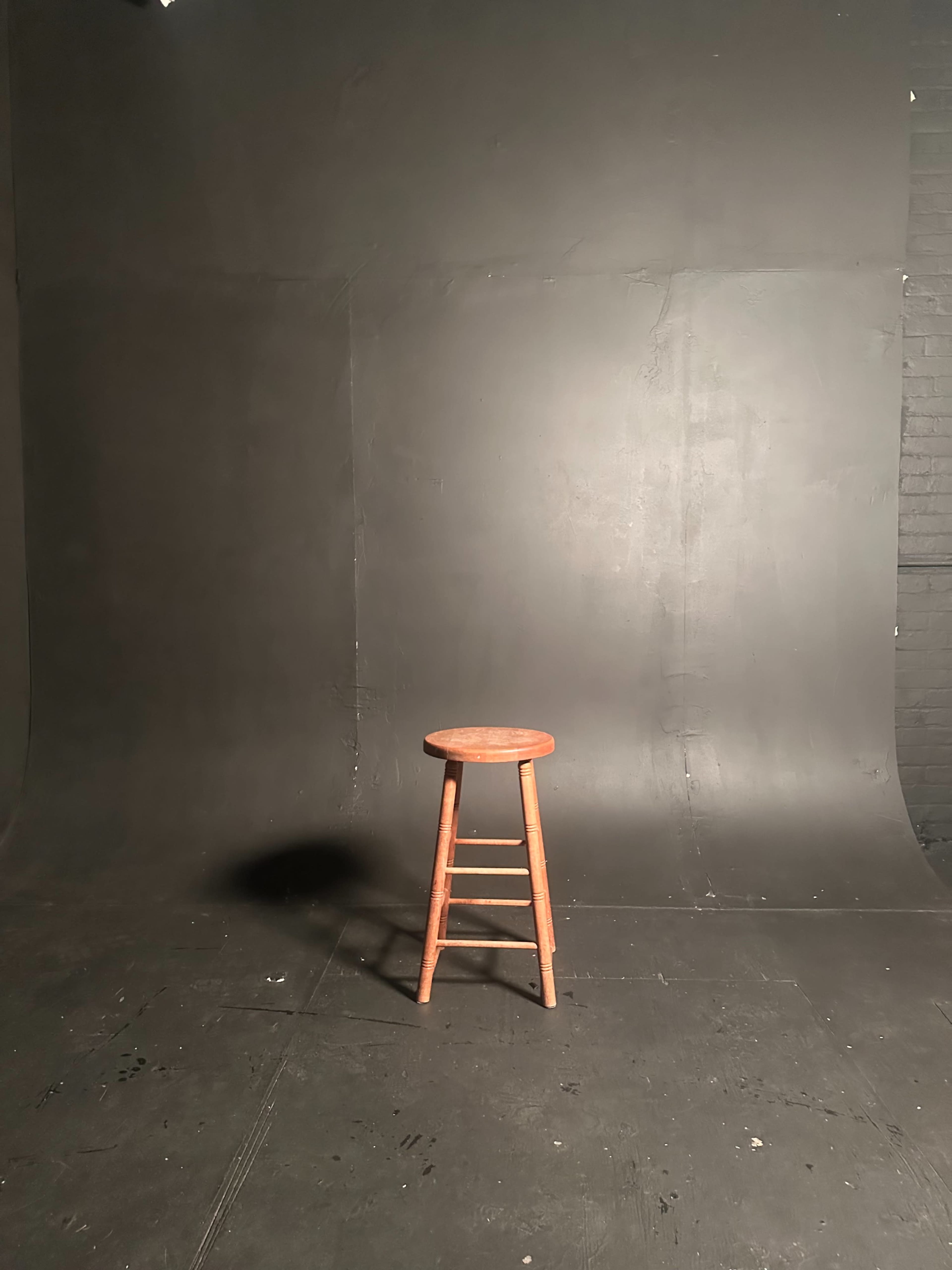 A wooden stool is positioned in front of a plain black backdrop.