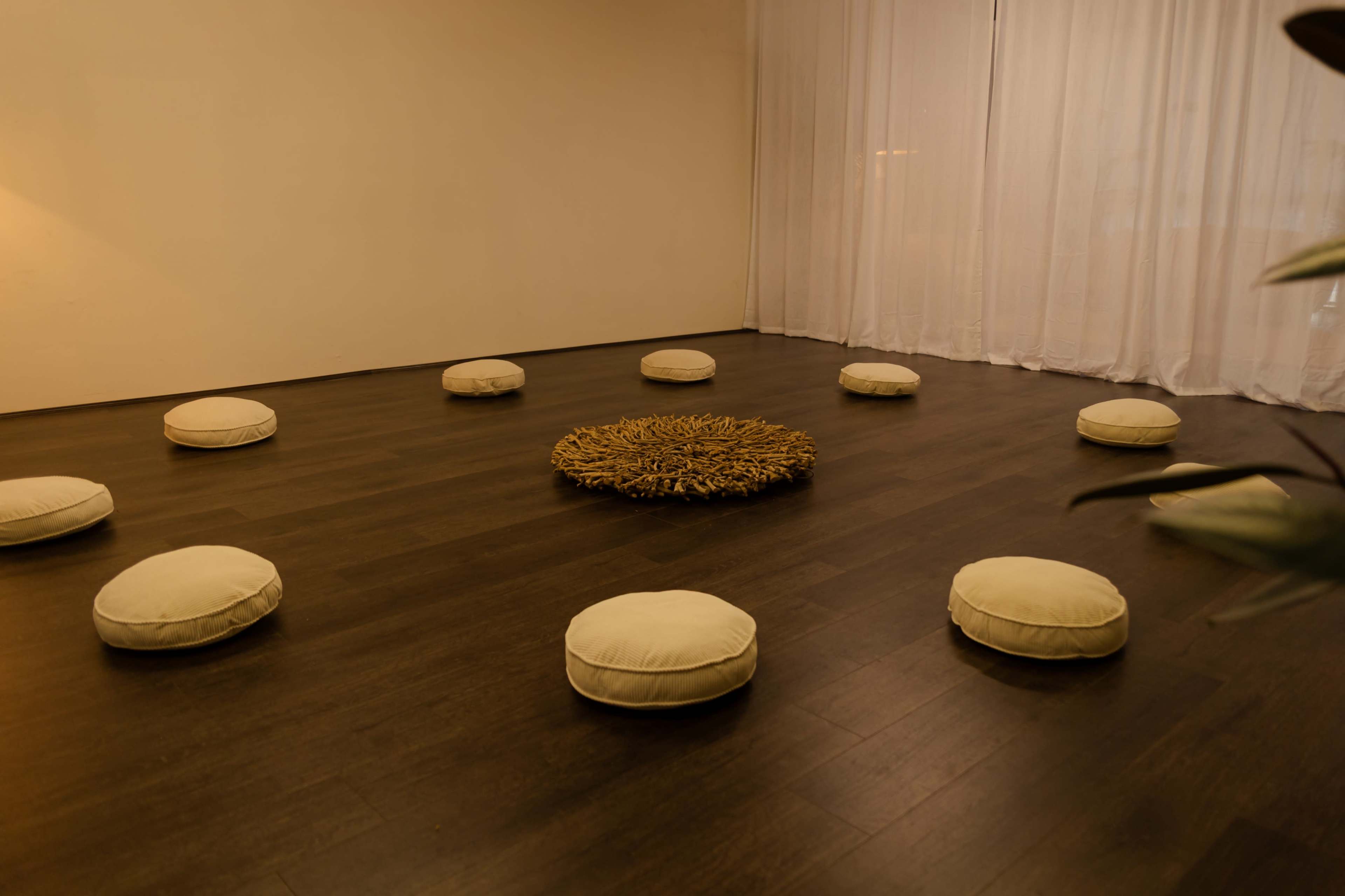 The image shows a medium-sized room with a wooden floor, featuring several round cushions arranged in a circular pattern around a central decorative piece made of natural materials.