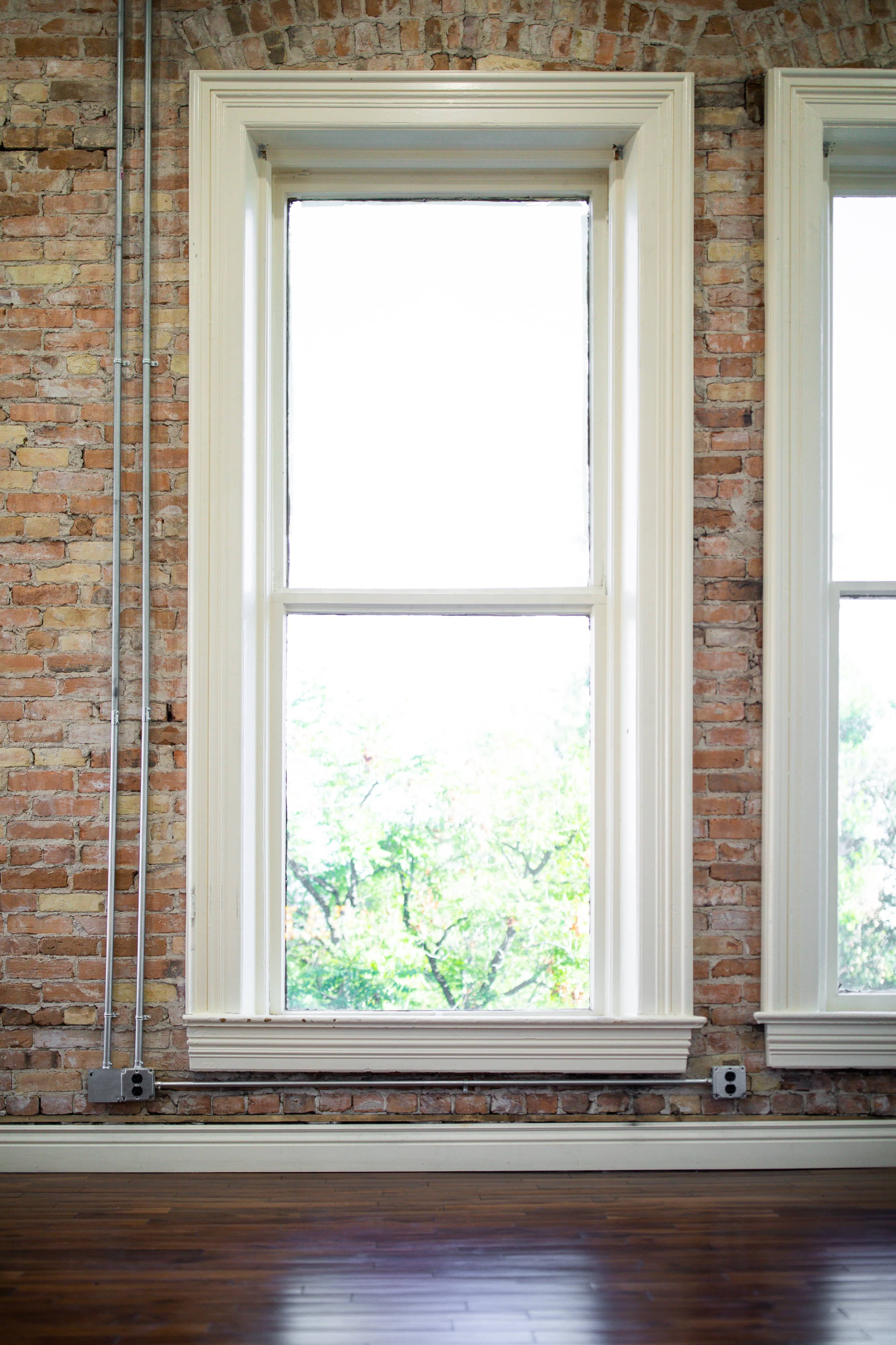 A large window with white trim is set in a brick wall, looking out onto greenery outside.