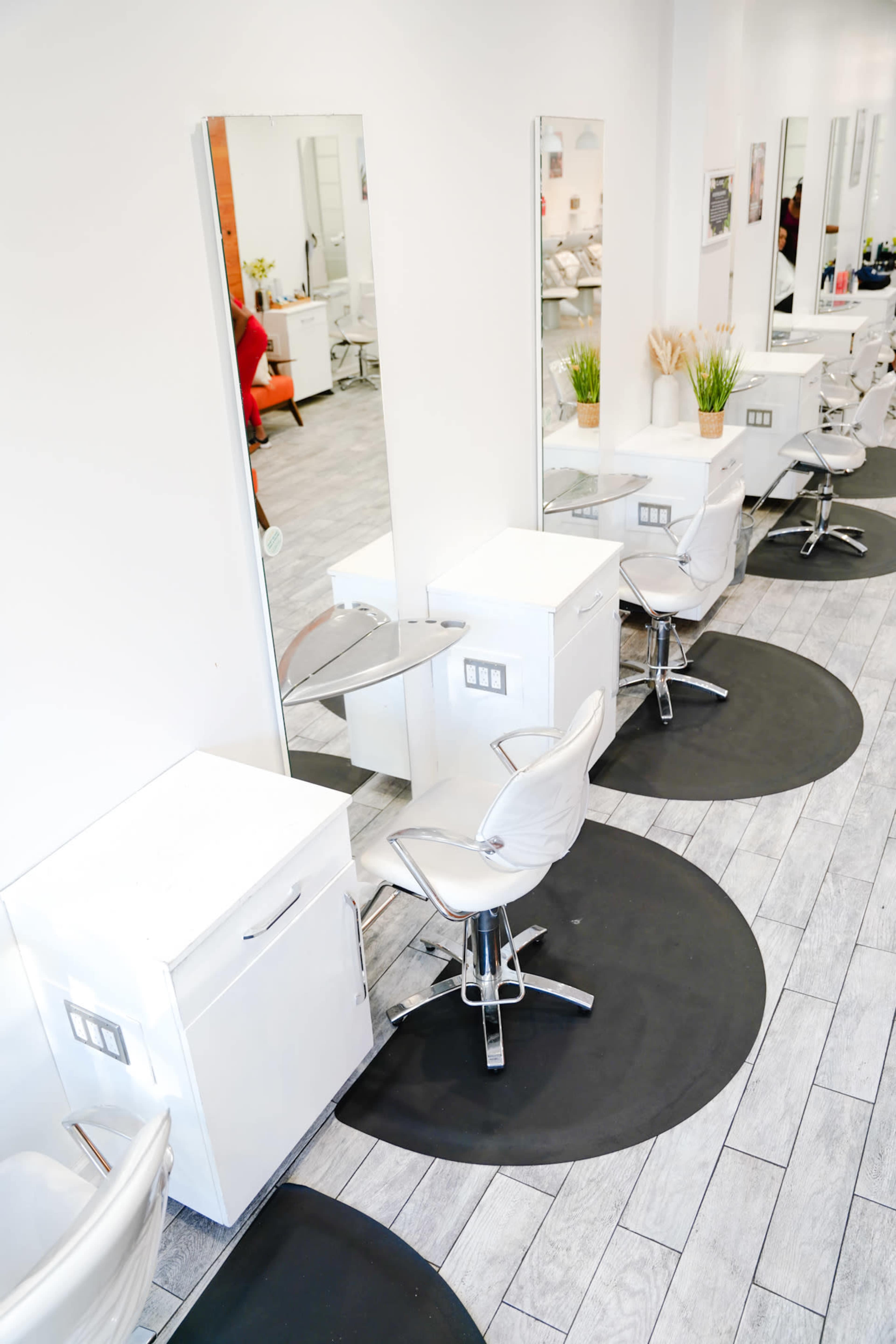 A modern hair salon with white styling stations and black circular mats on a wooden floor.