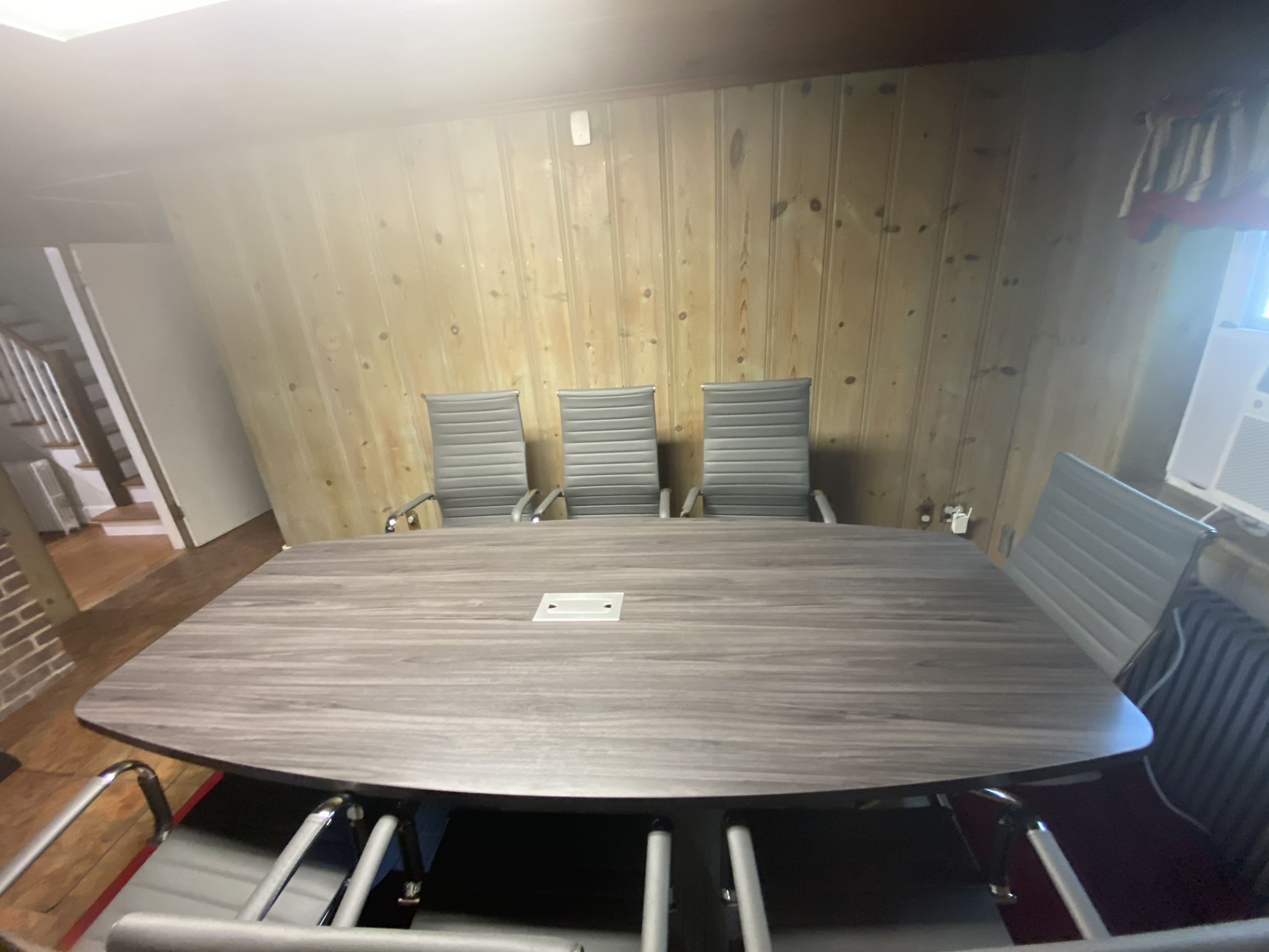 A conference room with a large wooden table surrounded by four modern metal chairs, set against a panelled wall.