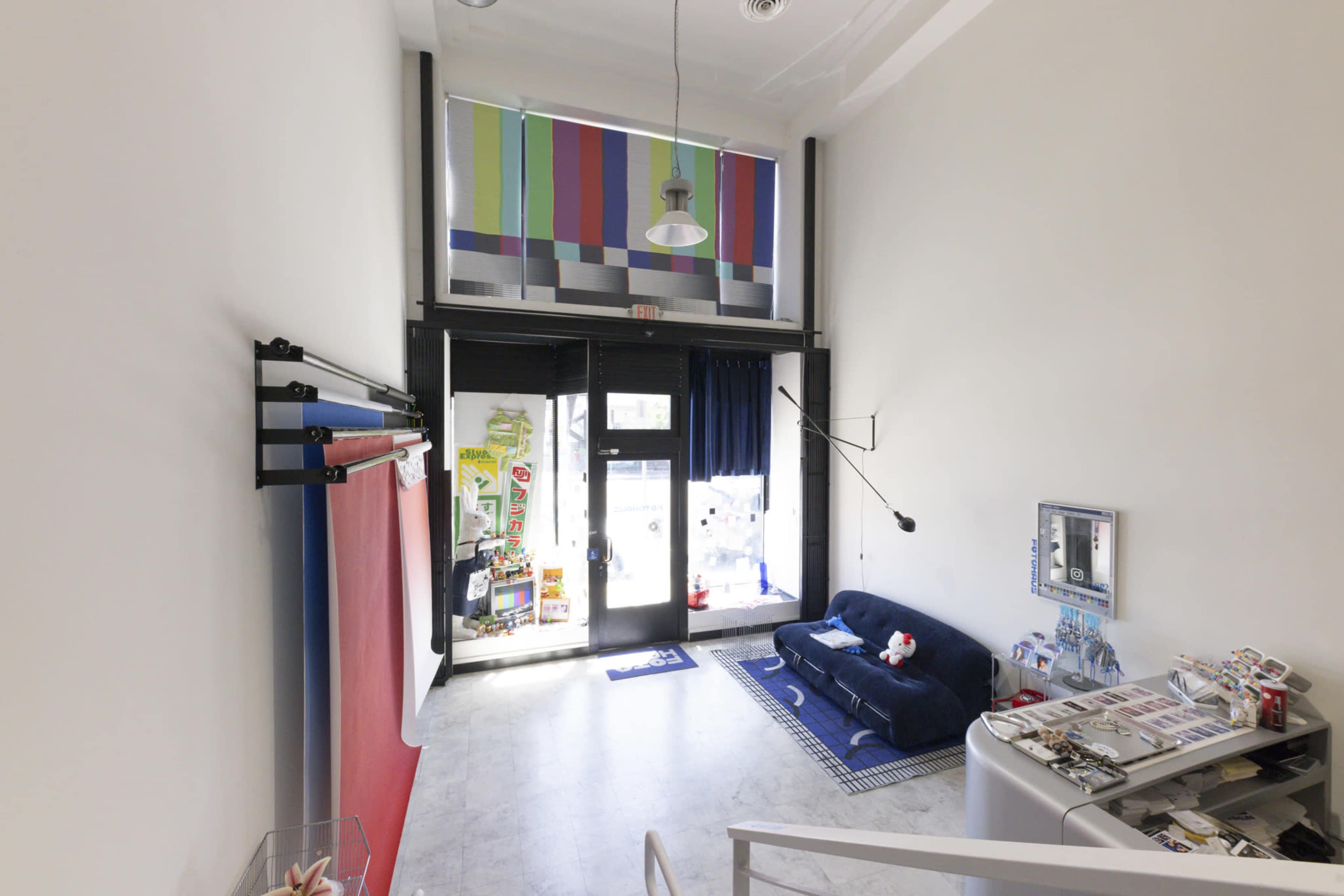 The image shows a modern interior of a storefront with a blue couch, colorful vertical art on the wall, and large glass doors leading outside.