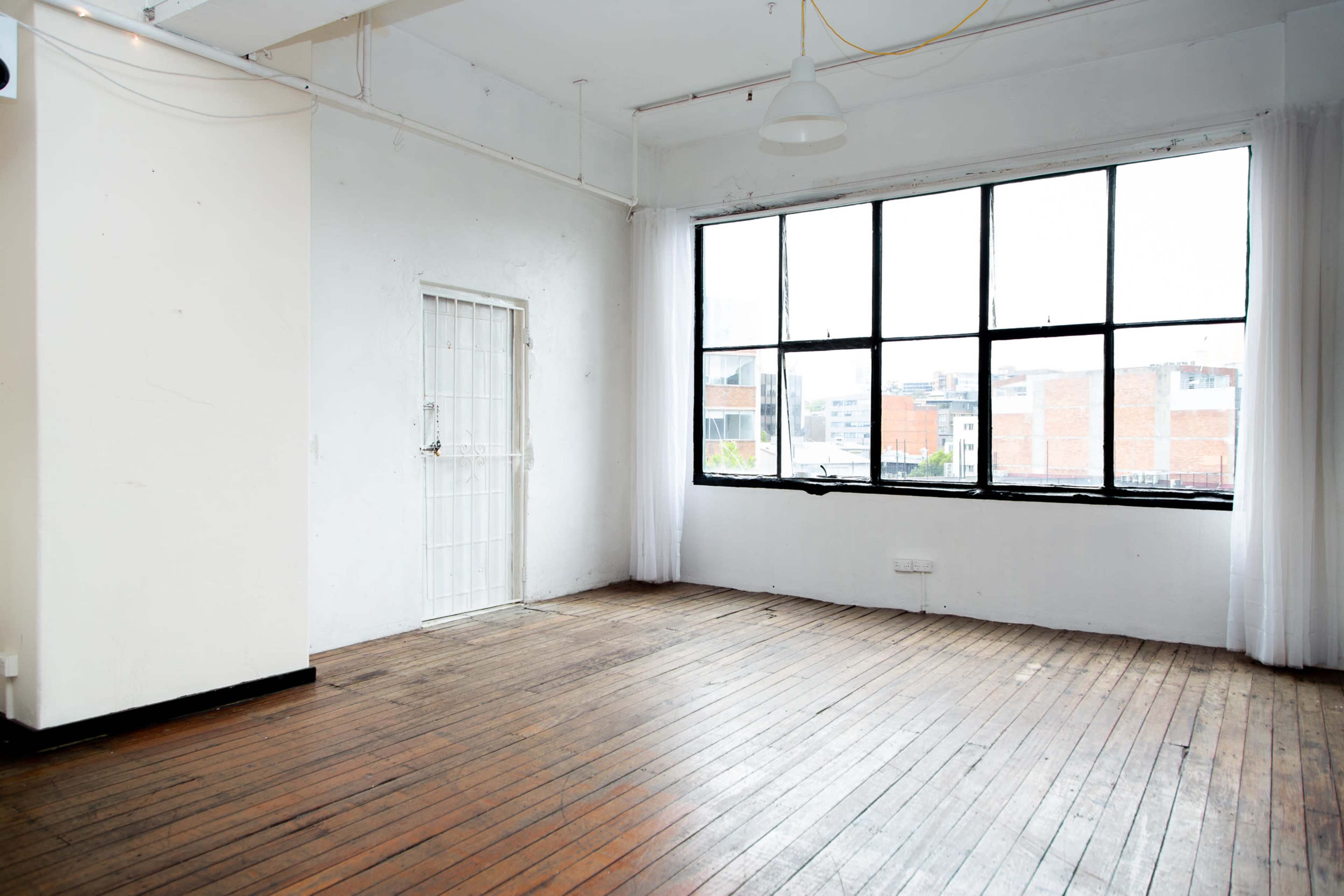 A spacious, empty room with large windows and exposed wooden floors.