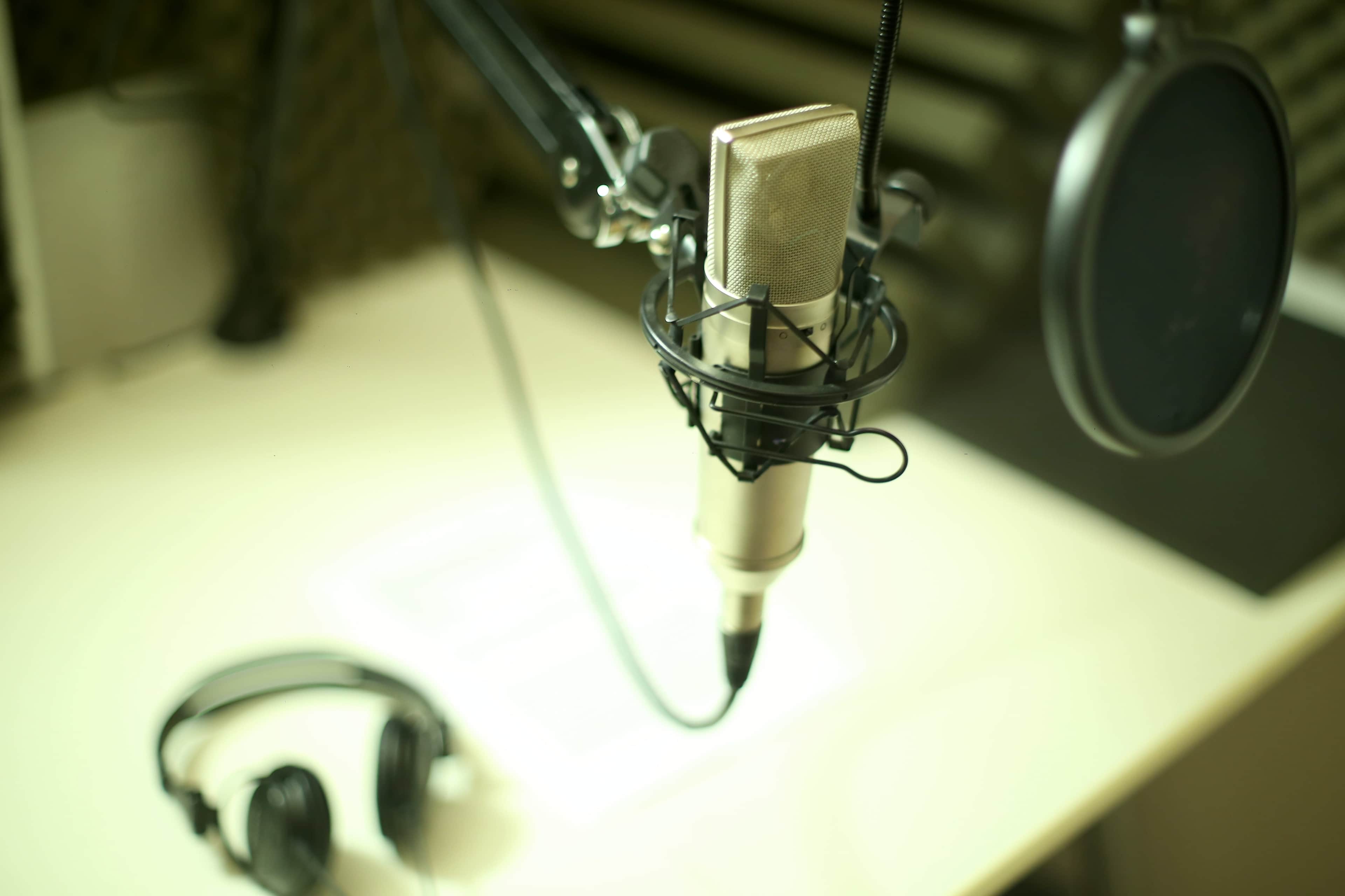A microphone is positioned on a stand beside a pair of headphones on a desk in a sound studio.