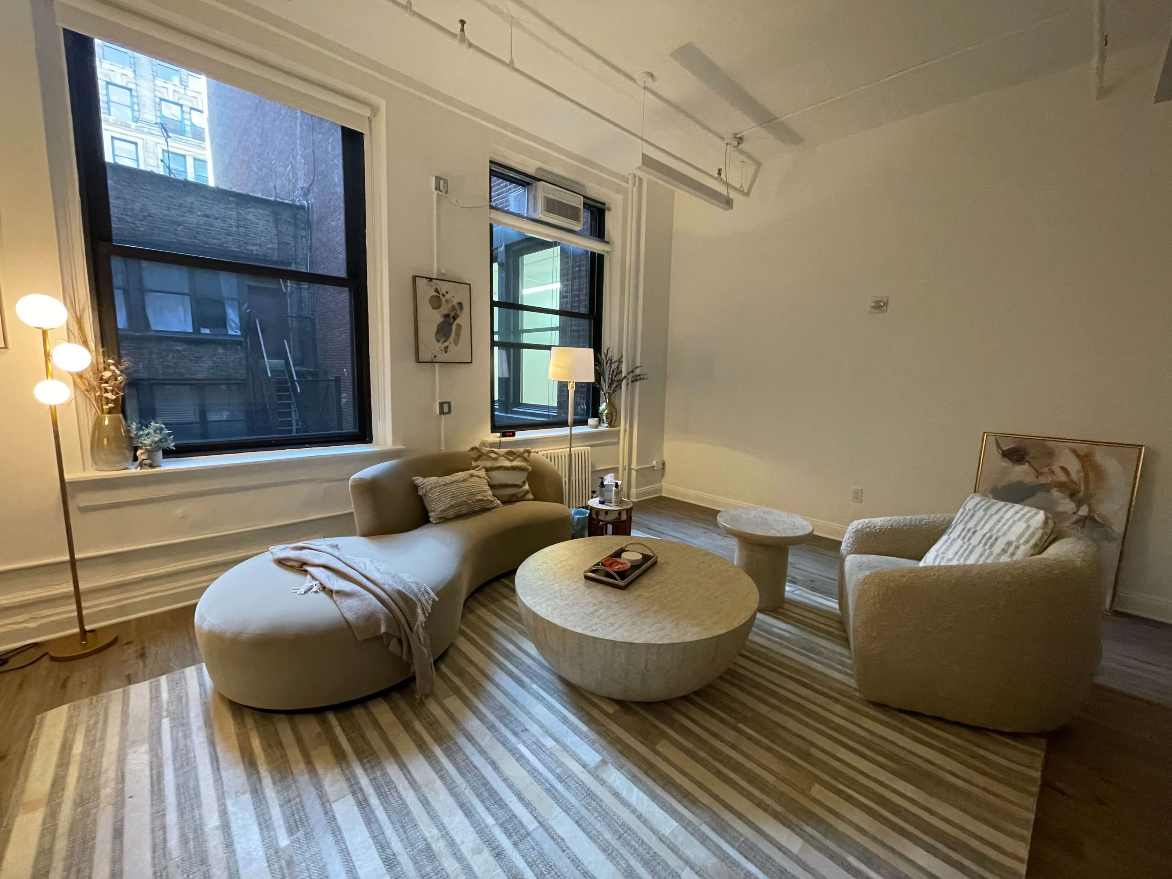A cozy living room features a curved sofa, a round coffee table, and large windows providing natural light.