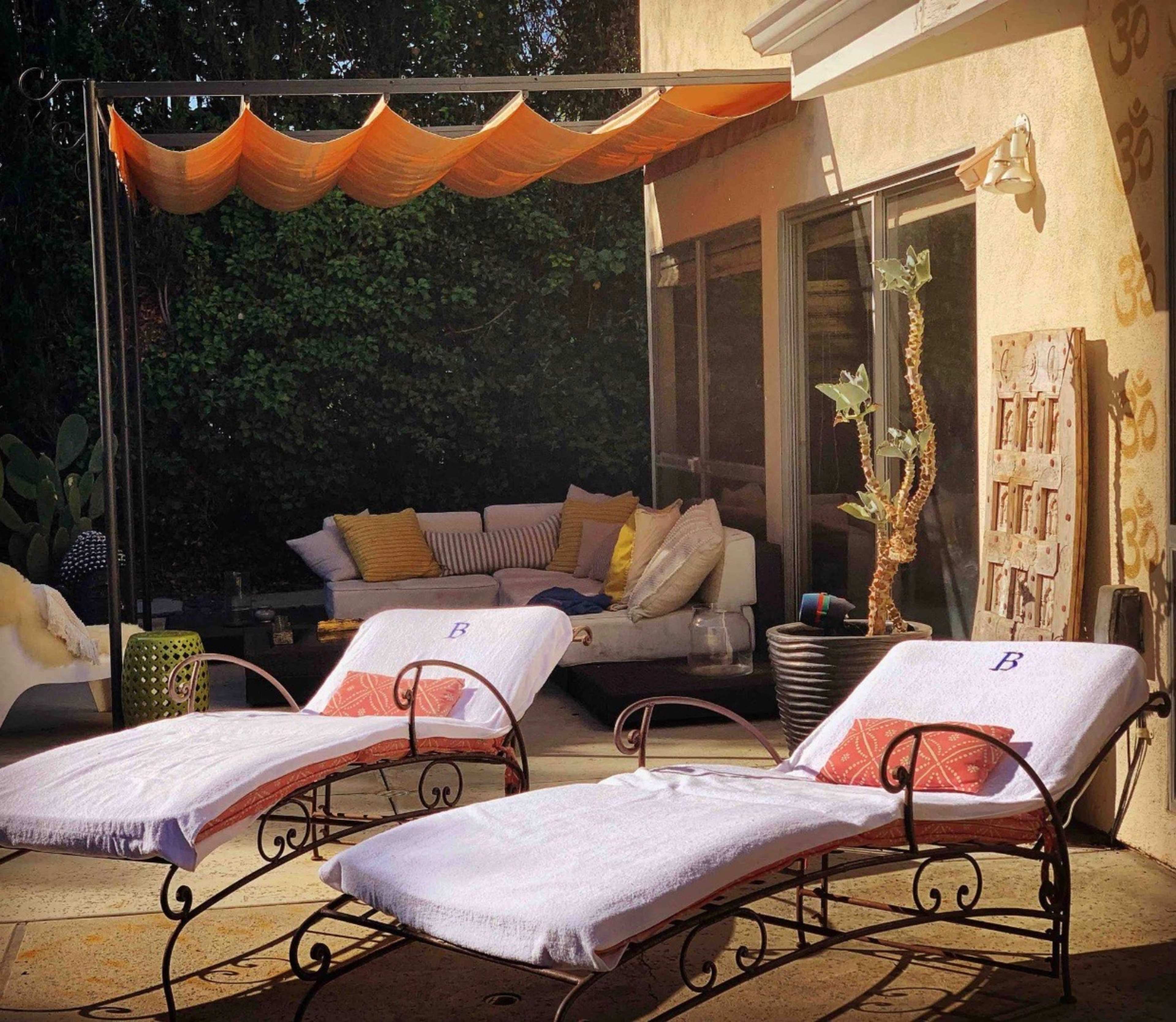 Two lounge chairs with white towels are positioned under a shaded area beside a seating arrangement and decorative elements in an outdoor space.