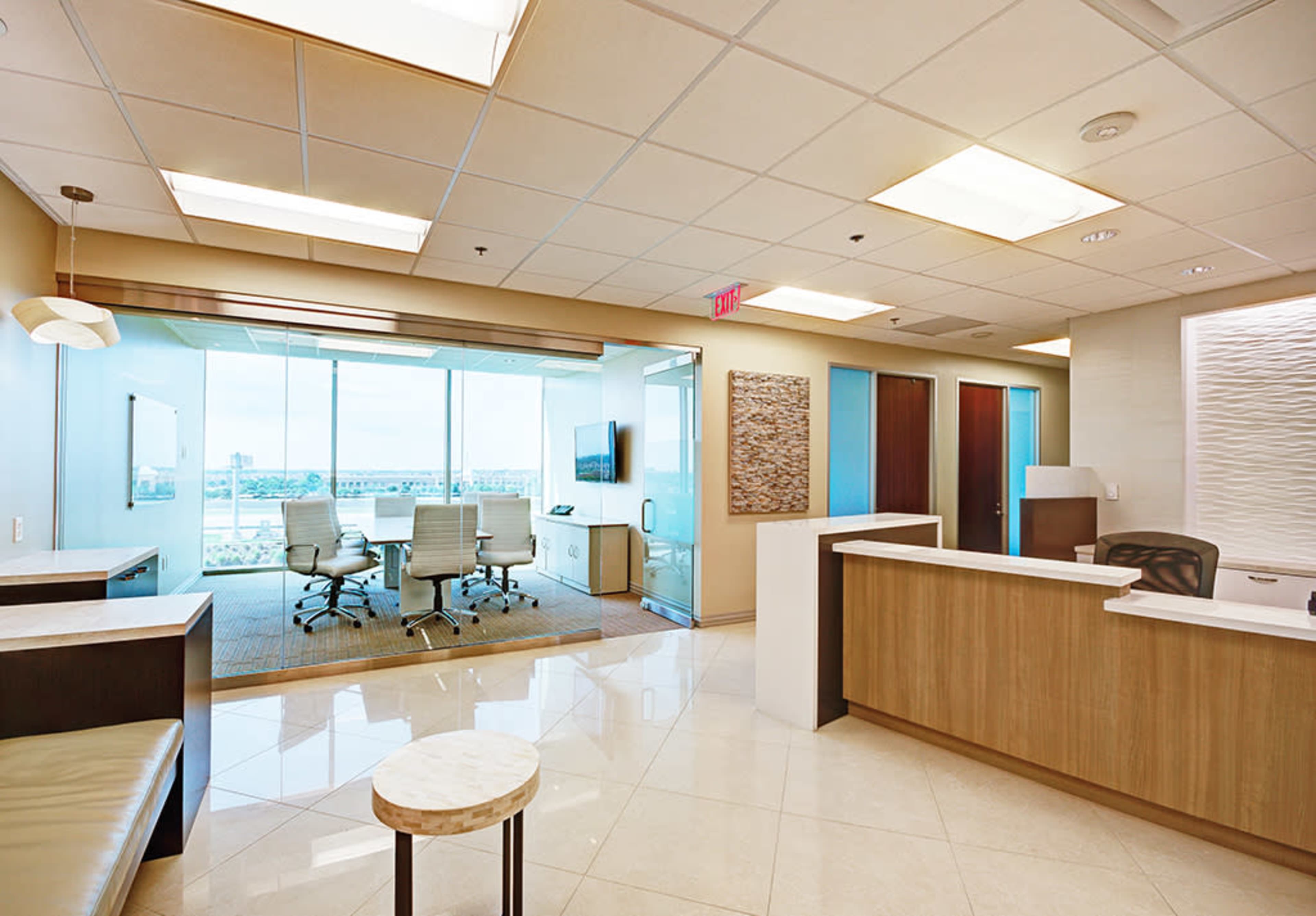 A modern office reception area with a seating area, a front desk, and a glass-walled conference room in the background.