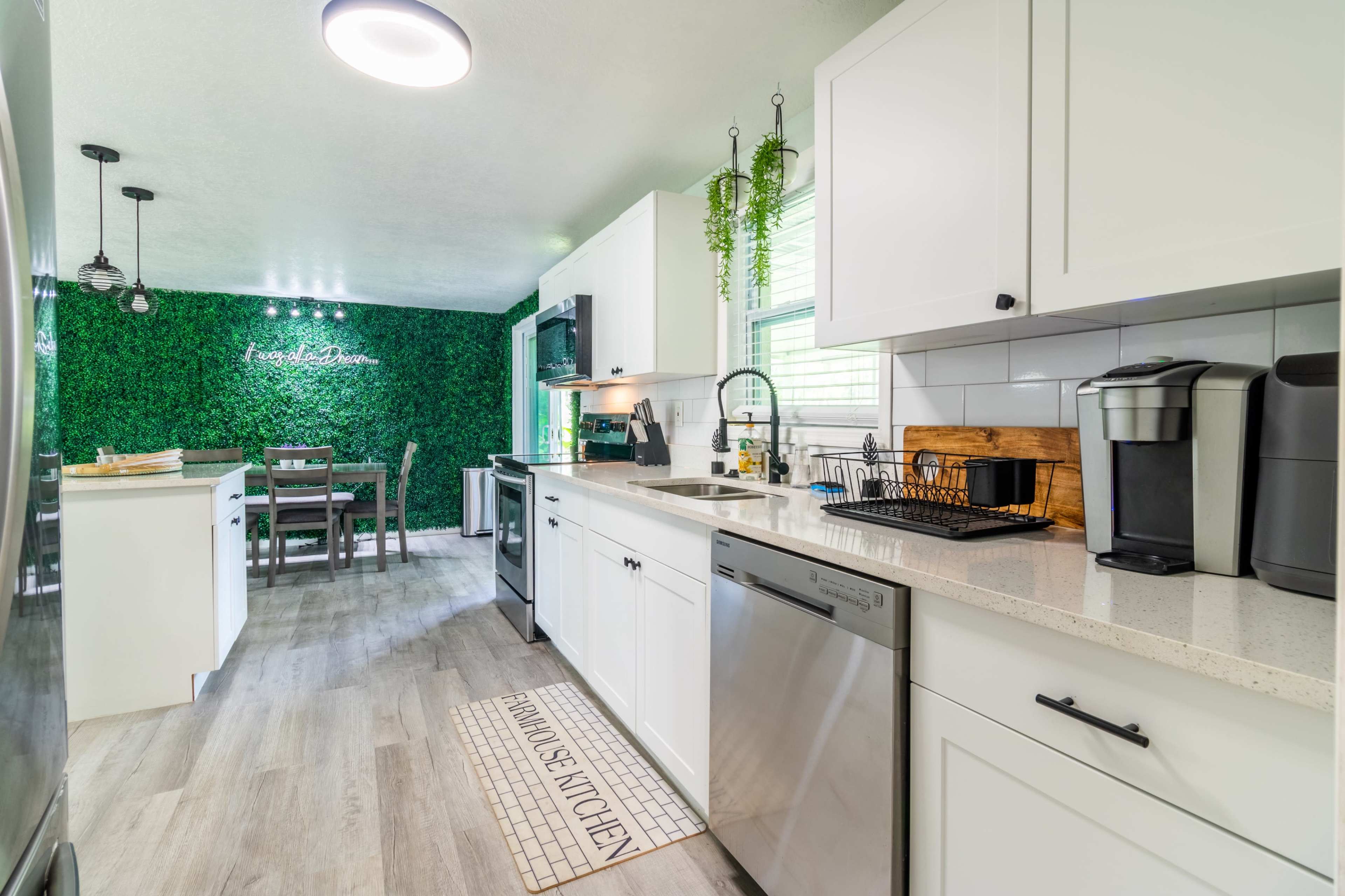 A modern kitchen with white cabinets, a countertop, and a dining area in the background, adorned with green wall decor.