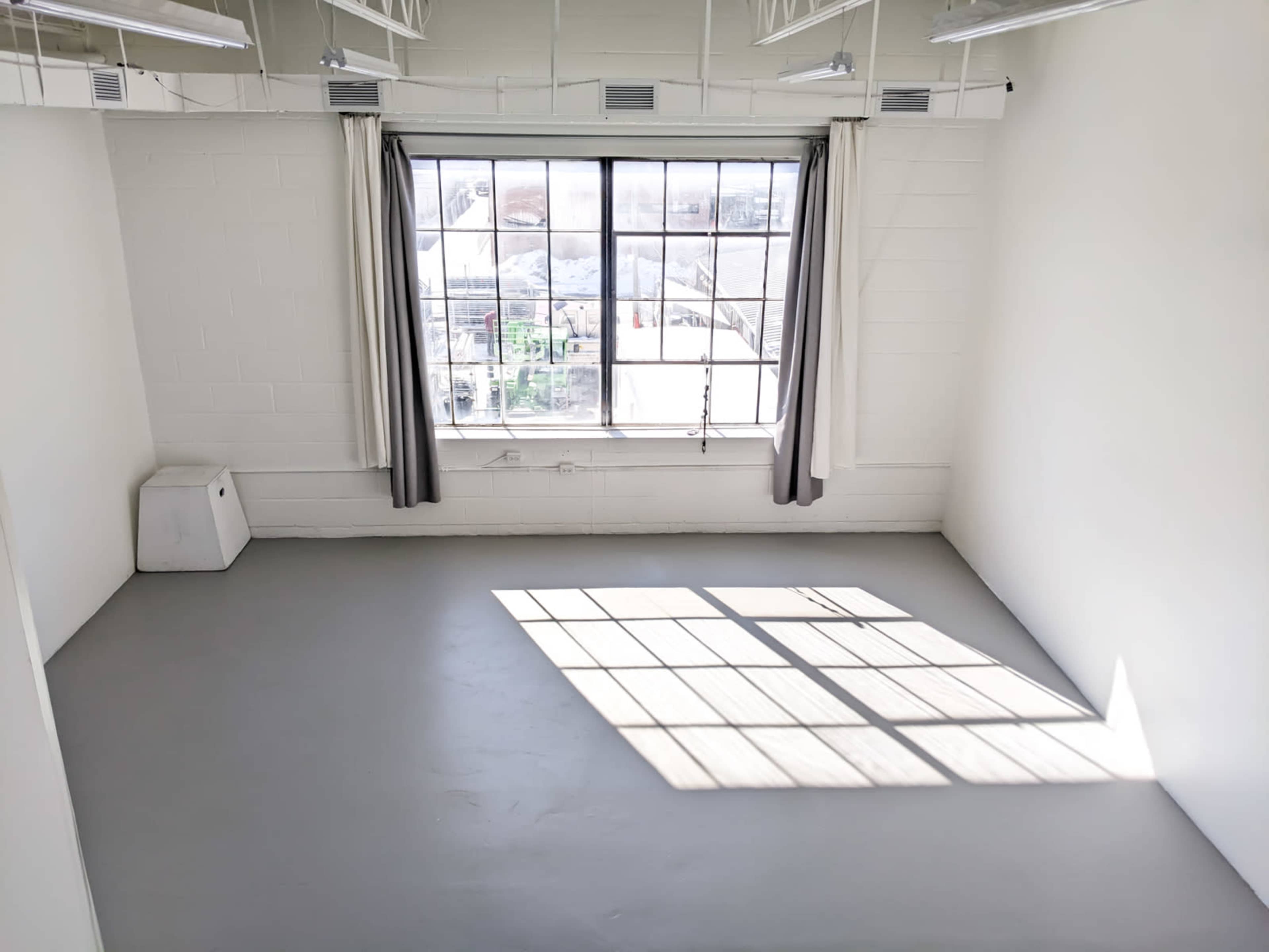 The image shows an empty room with gray flooring, a large window with curtains, and sunlight casting a rectangular shadow on the floor.