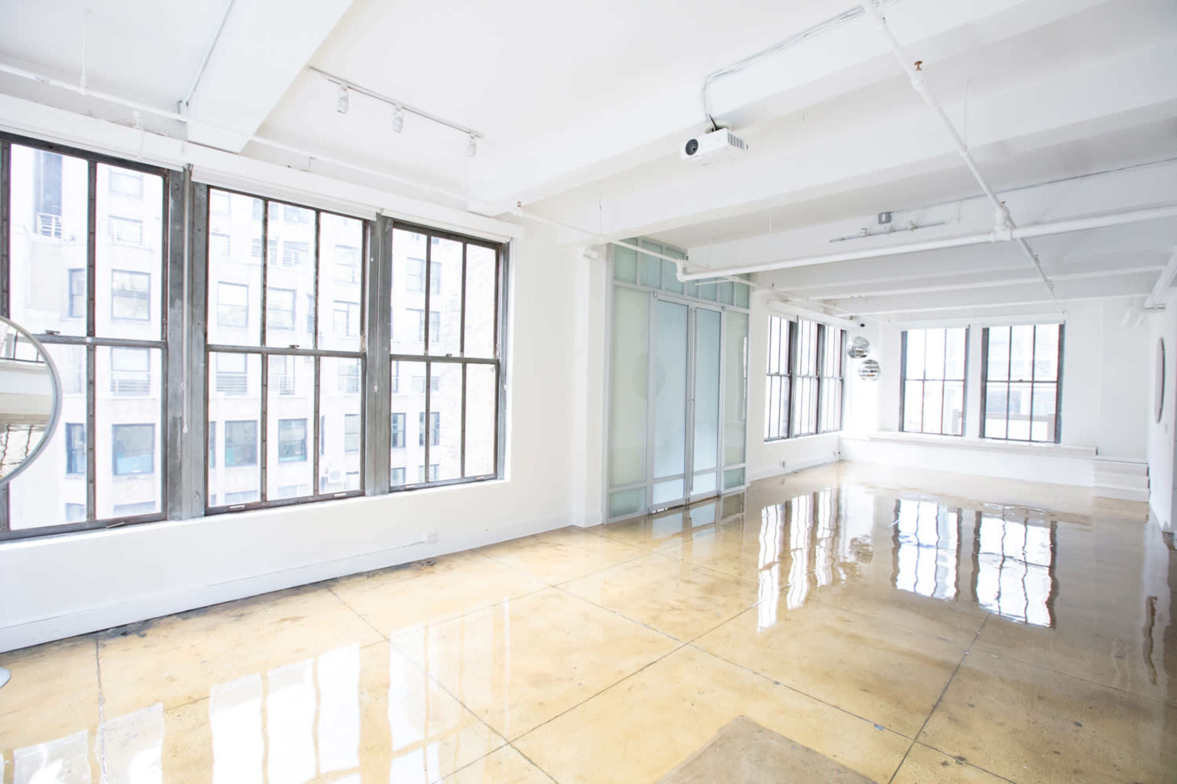 The image shows a spacious, bright room with large windows, polished concrete floors, and an open layout.