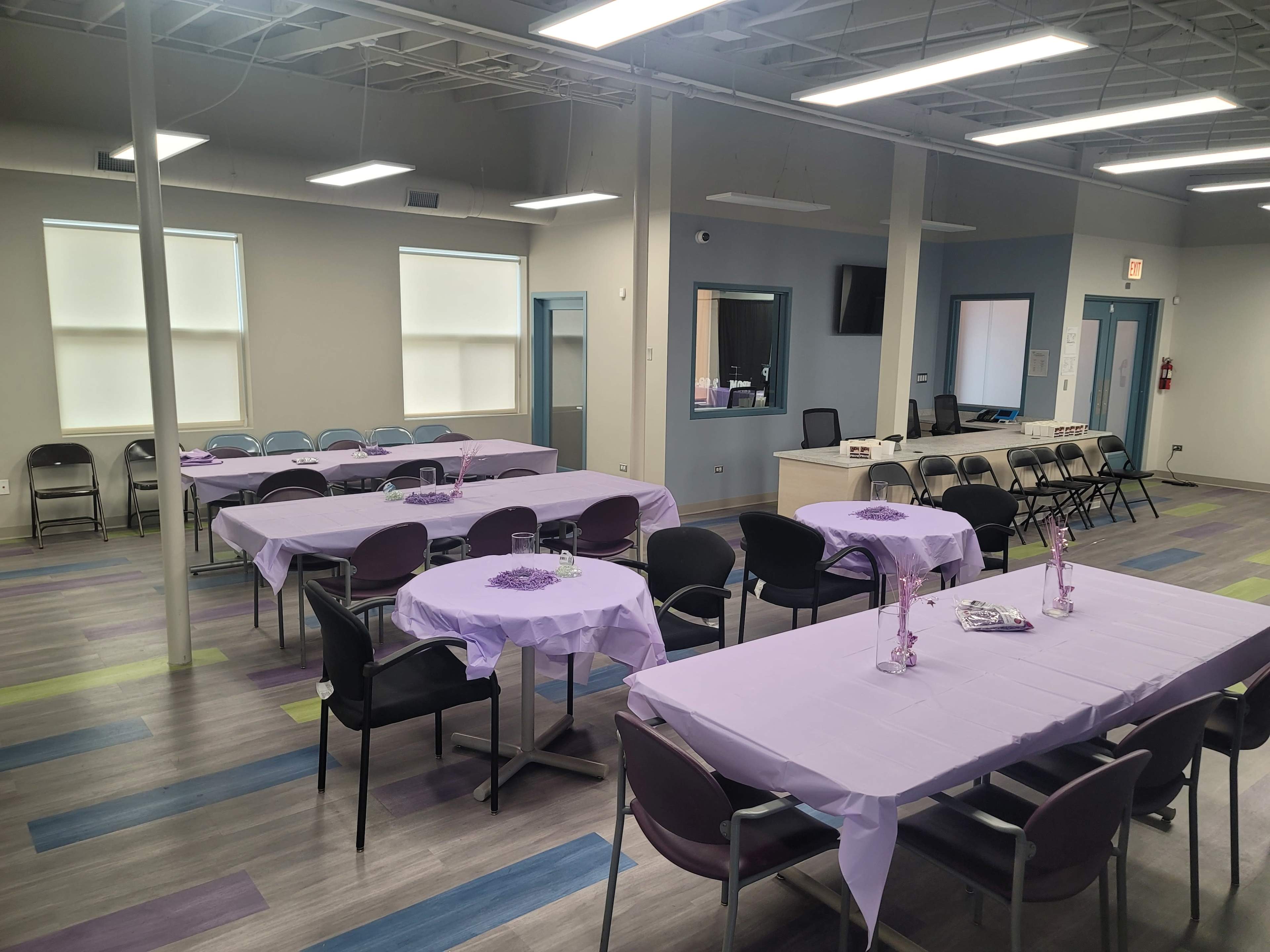 A spacious room arranged with tables covered in purple cloths and chairs set in an organized manner, ready for an event.