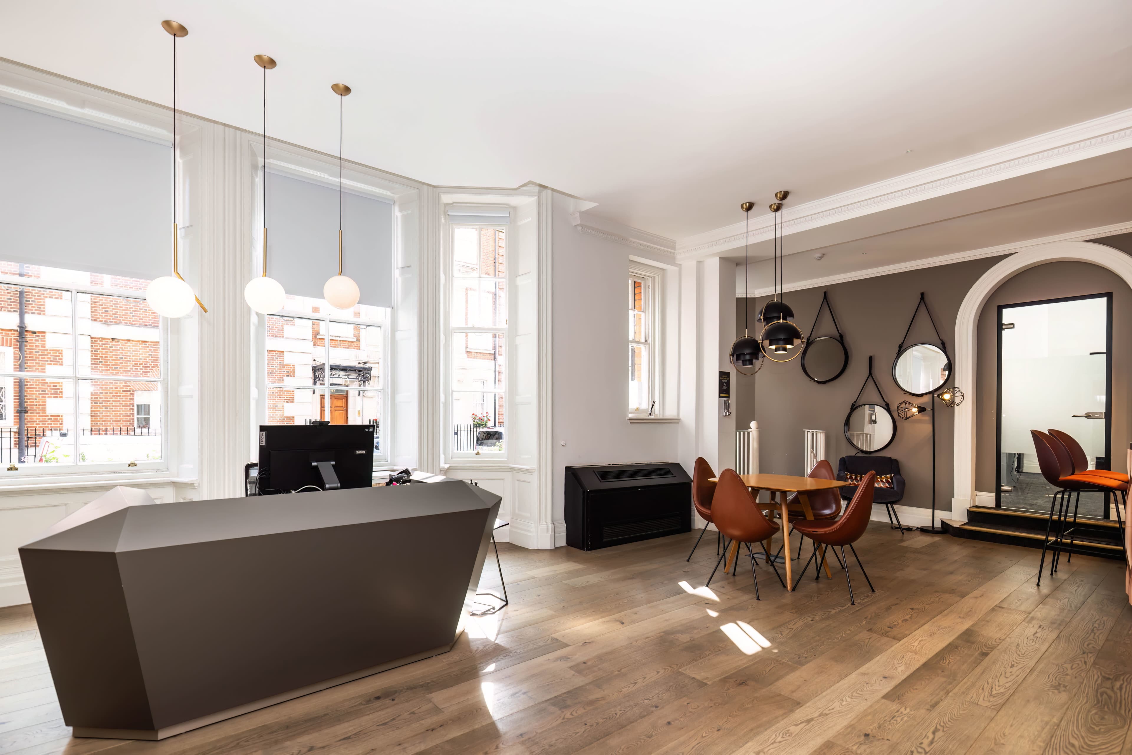 A modern office interior with a geometric reception desk, a dining area, and large windows allowing natural light to enter.