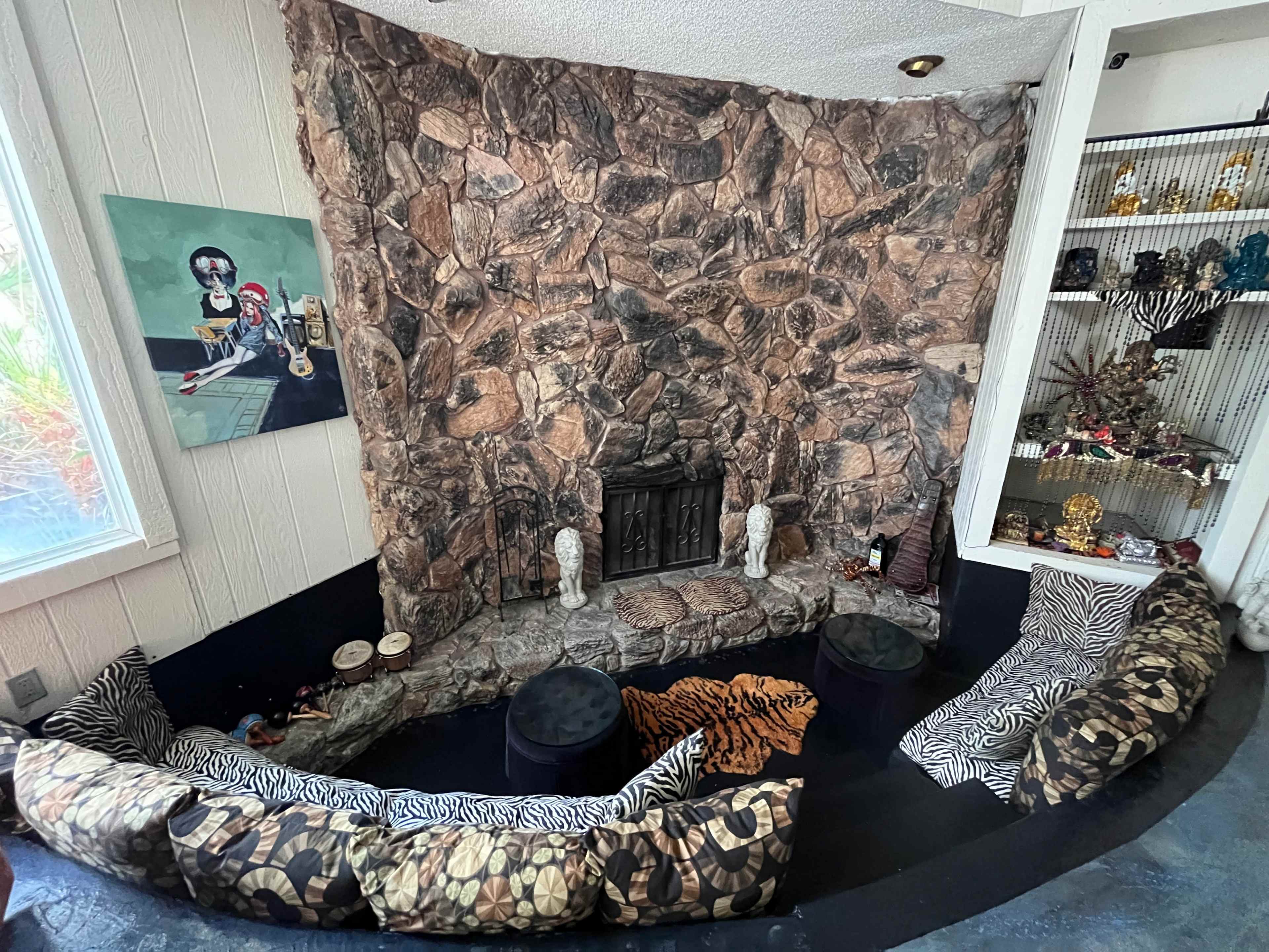 A curved seating area in front of a stone-faced fireplace, accented by decorative pillows and a small display shelf nearby.