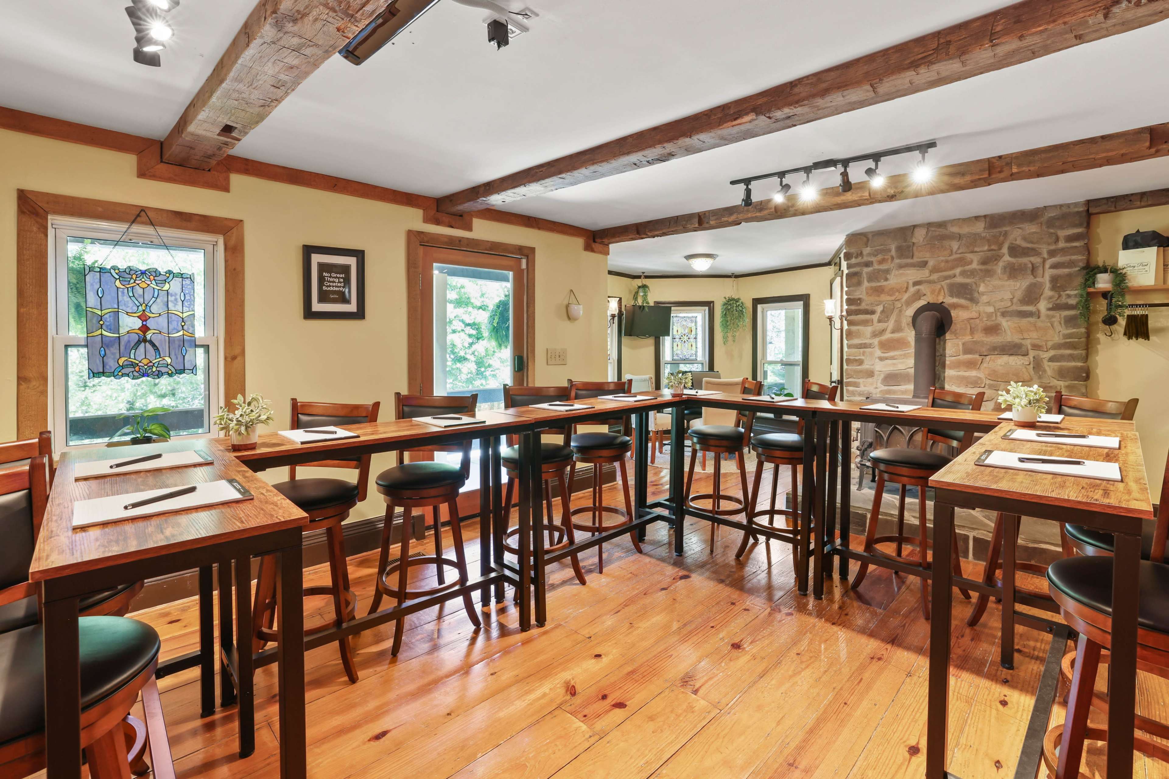 A cozy dining area features wooden beams, tall tables with stools, and large windows overlooking greenery.