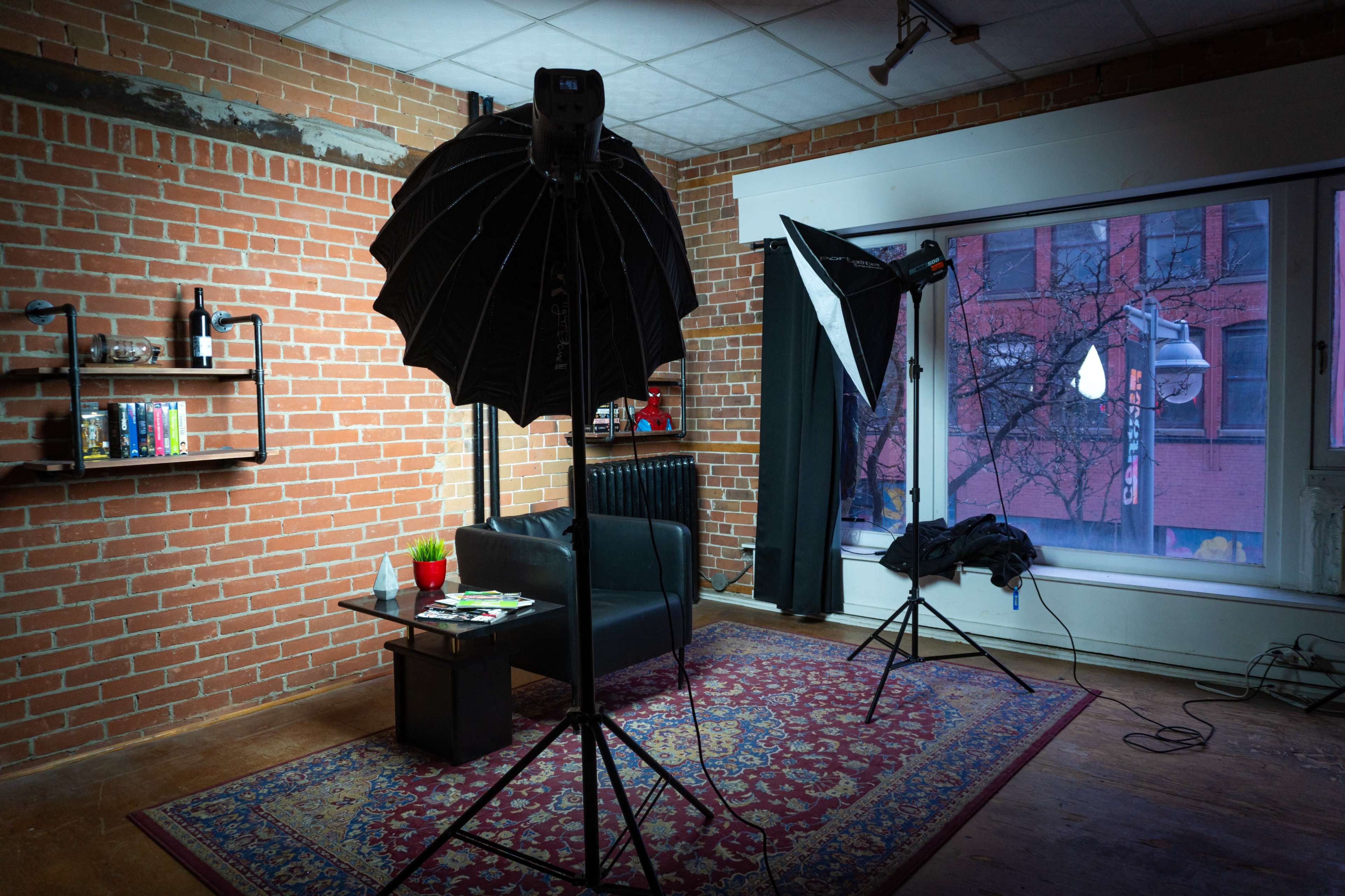 A room with exposed brick walls, featuring a black couch, a small coffee table, and two lighting setups near a window.