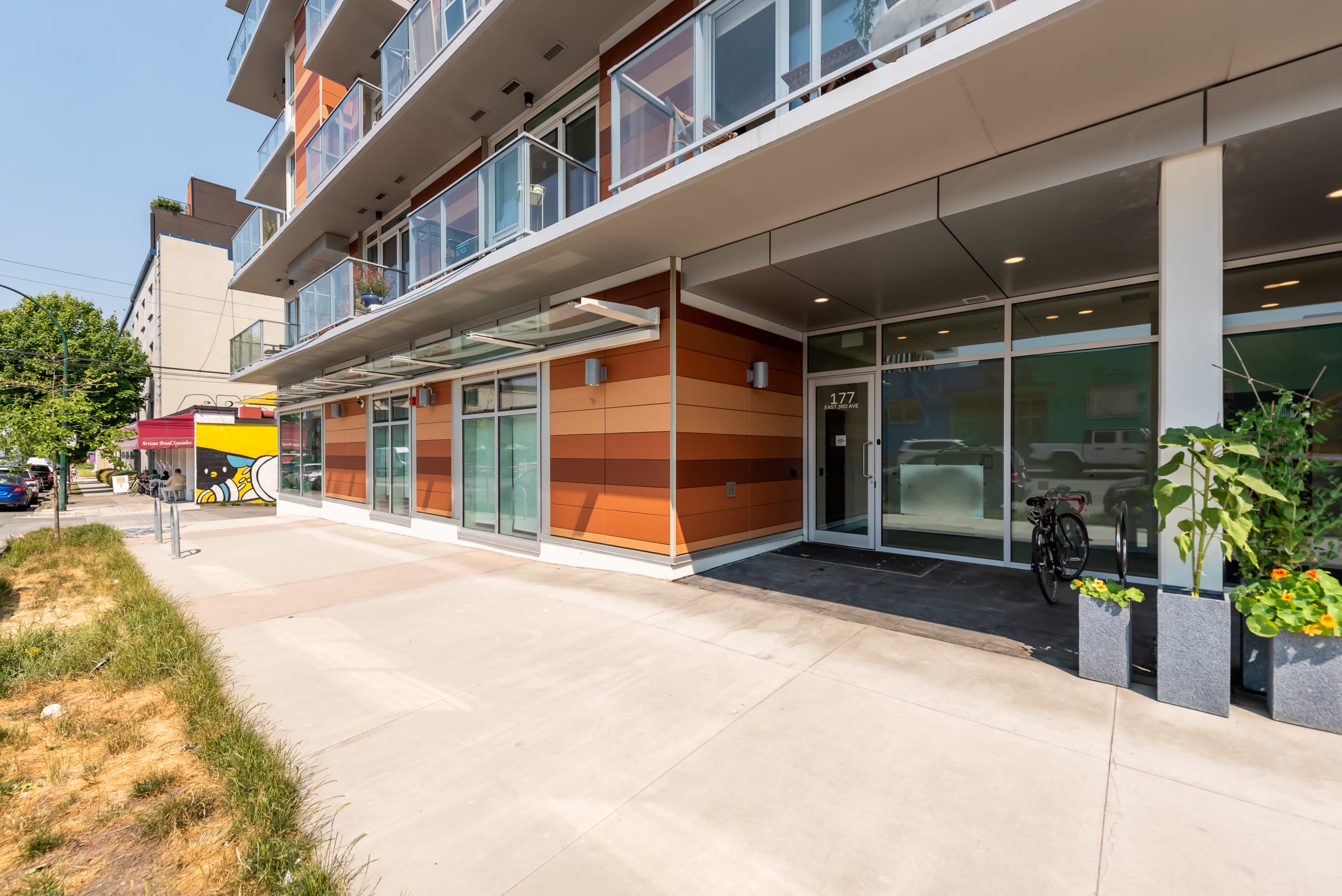 The entrance of a modern building with orange and gray paneling, featuring large glass windows and a bike parked outside.