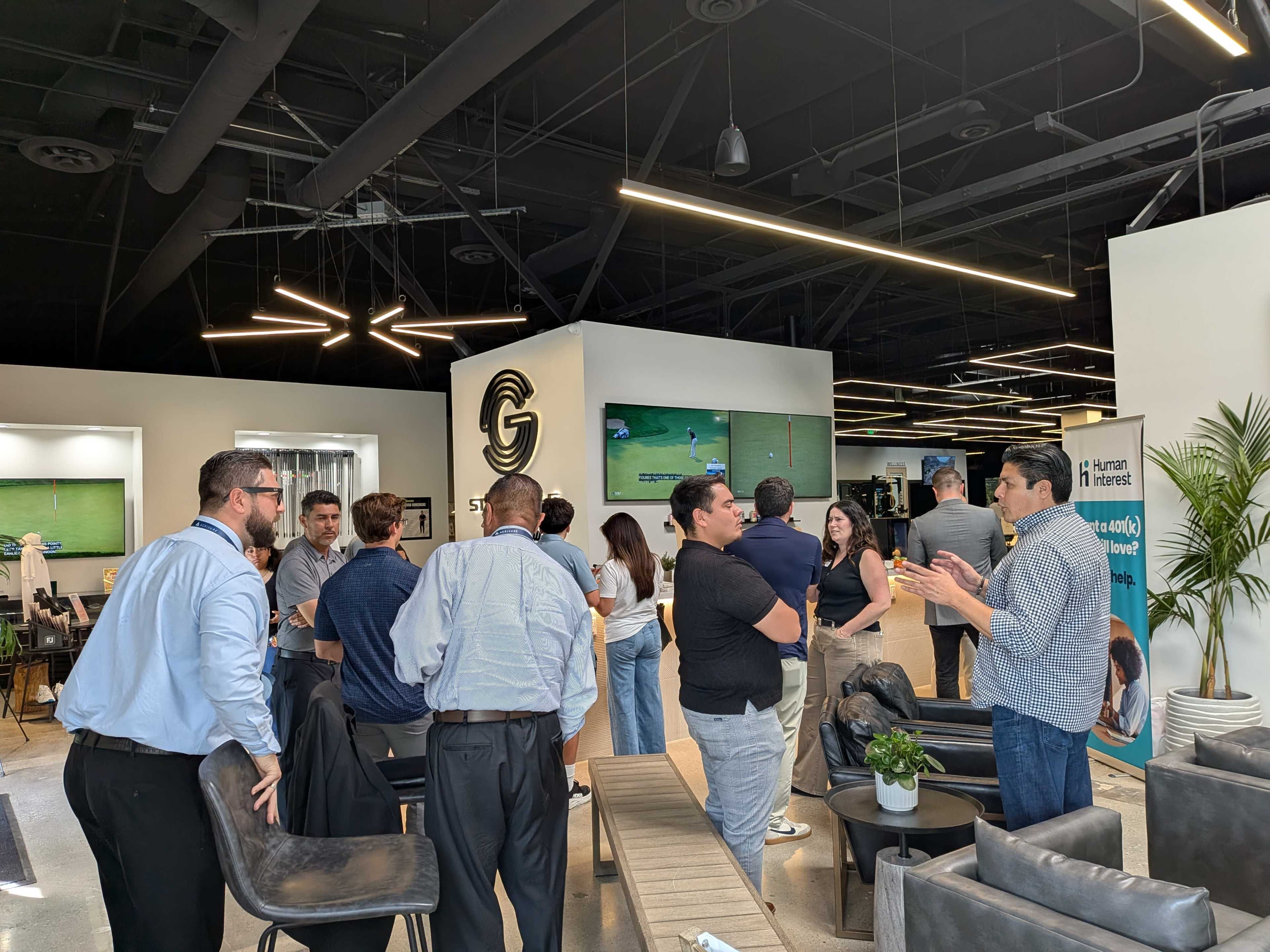 A group of people is gathered in a modern office space with televisions mounted on the walls and contemporary furnishings.