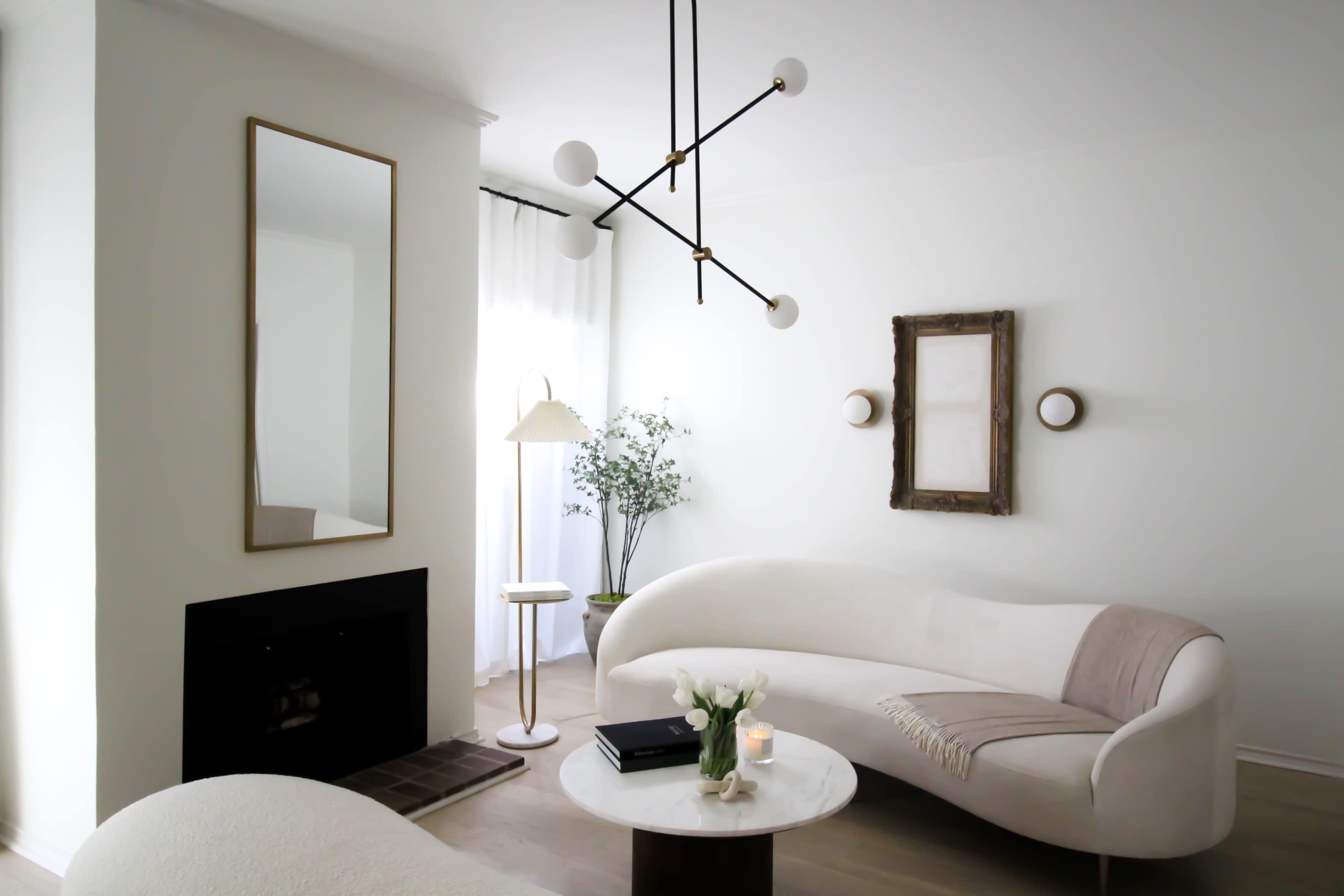 A light, modern living room with a curved sofa, a round coffee table, and a floor lamp, accompanied by decorative elements and a minimalist aesthetic.