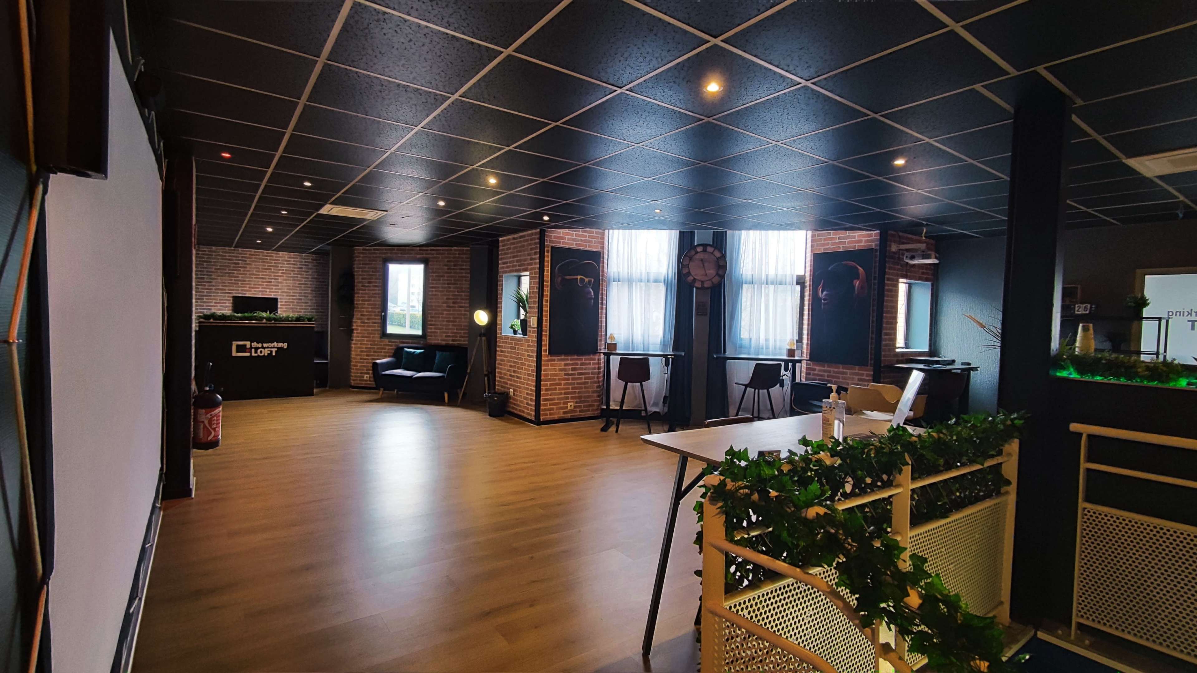 A spacious office interior with a reception area, seating arrangements, large windows, and a table decorated with greenery.