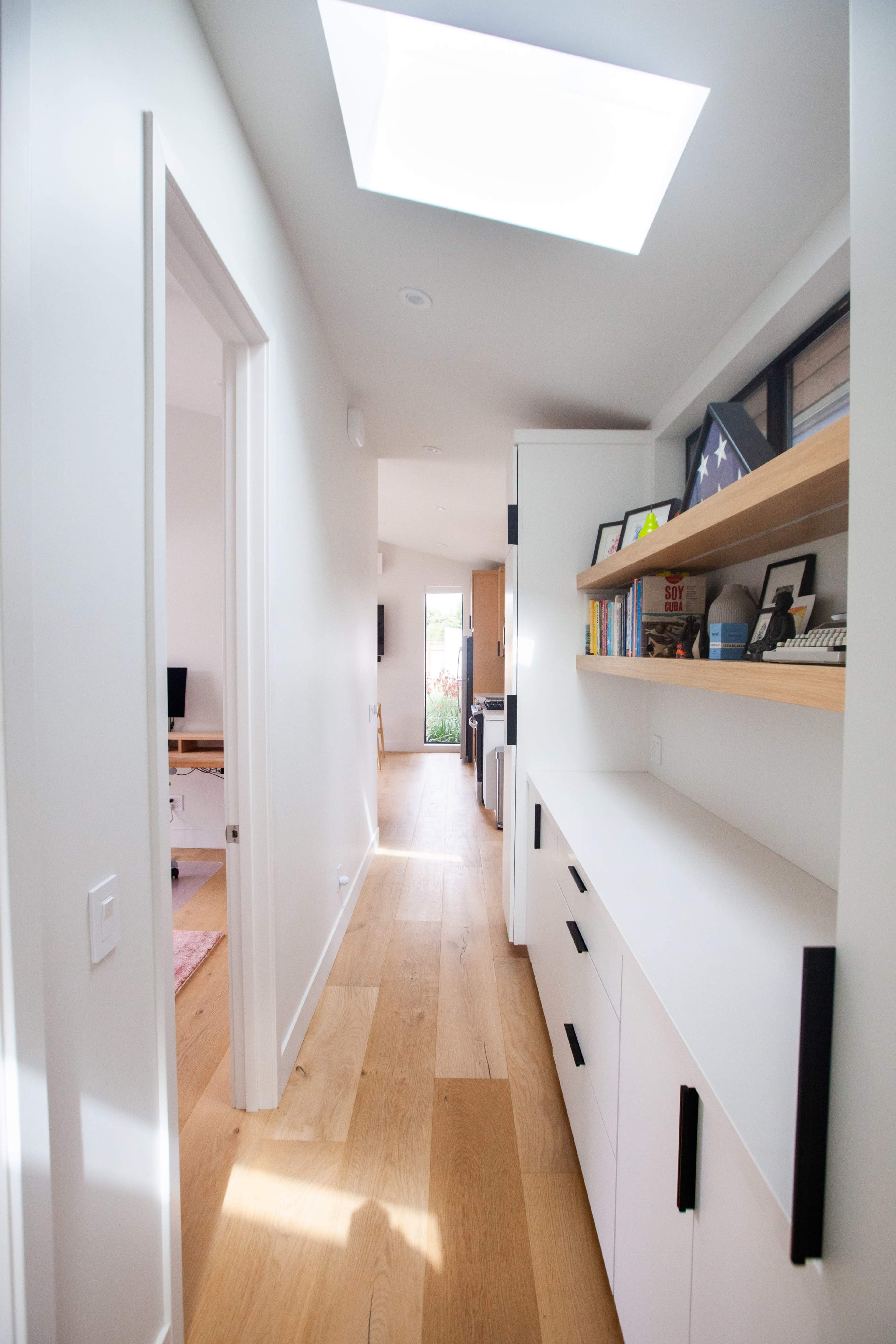 A bright hallway with a skylight features built-in shelves and a view of an outdoor space at the end.