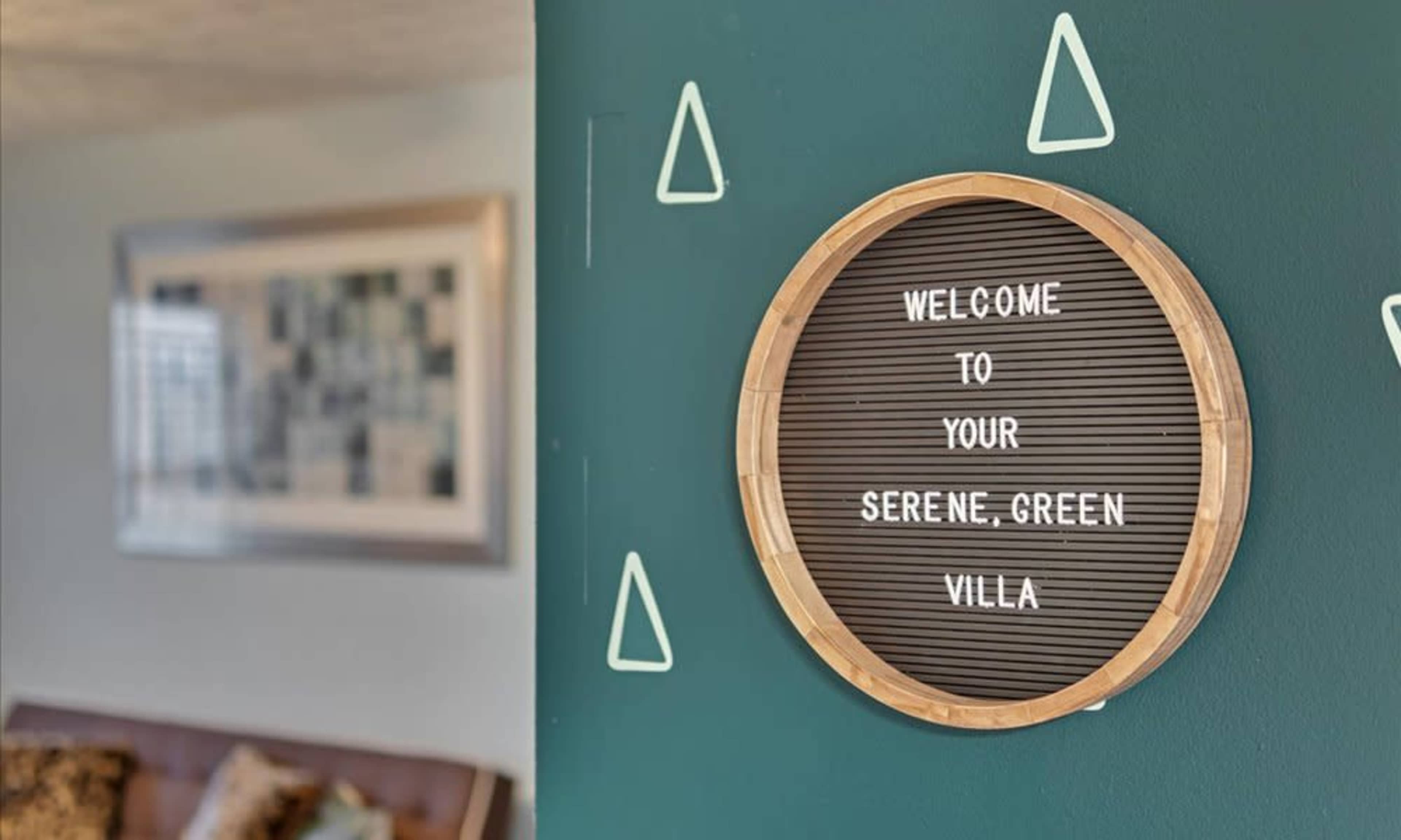 A round sign on a green wall reads "Welcome to your Serene Green Villa."