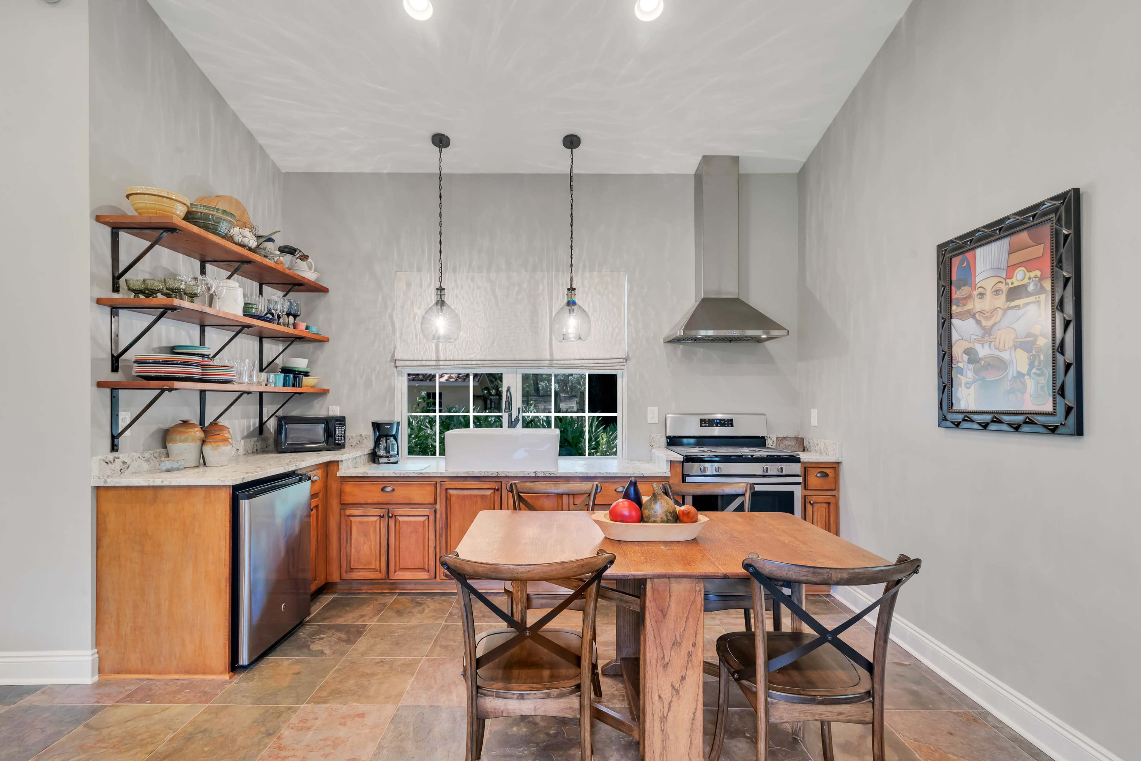 A well-organized kitchen features wooden cabinets, a stainless steel stove, and a dining table with chairs, illuminated by pendant lights.