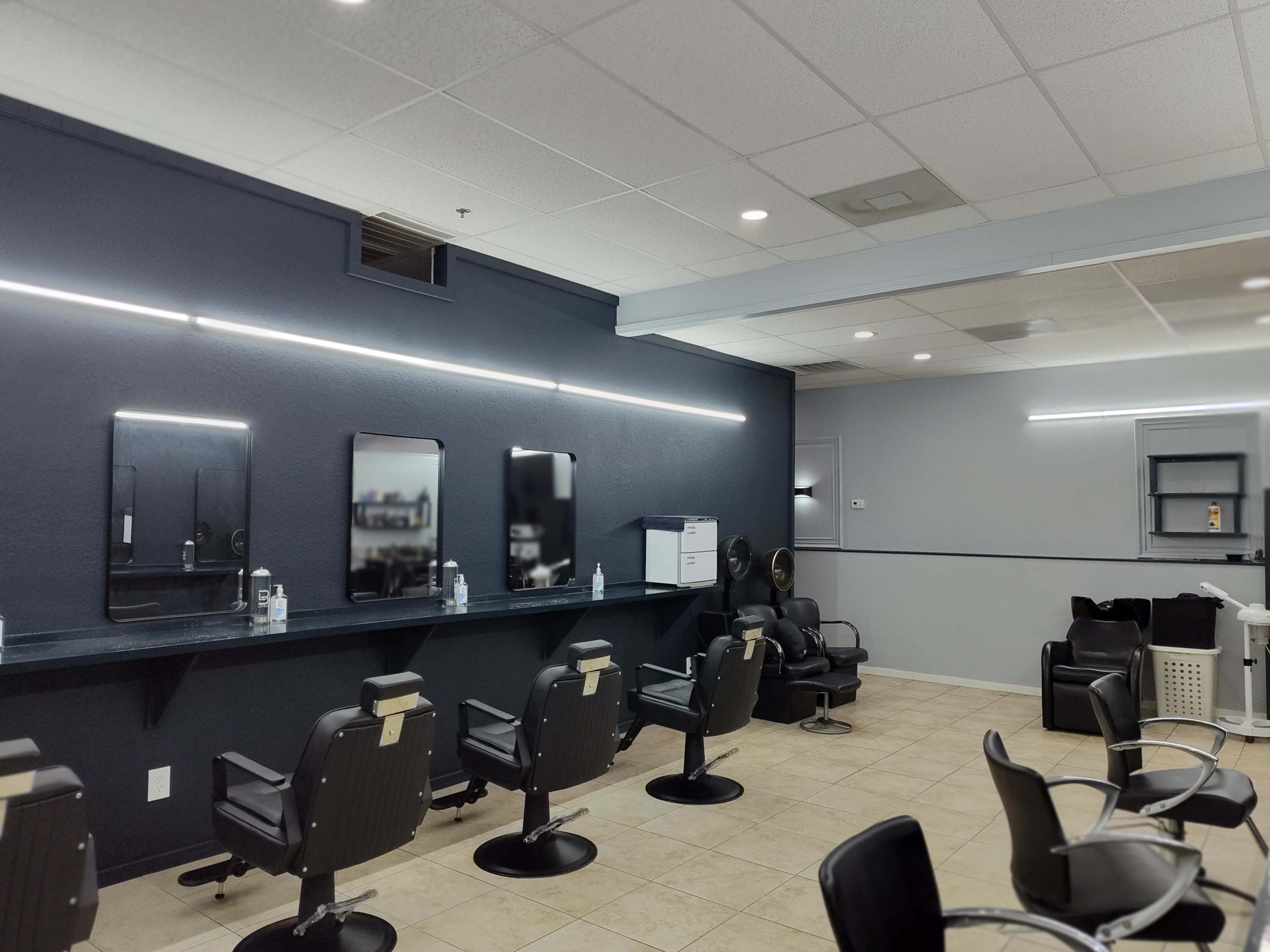A hair salon featuring several black barber chairs, mirrors mounted on the wall, and a clean, organized layout.