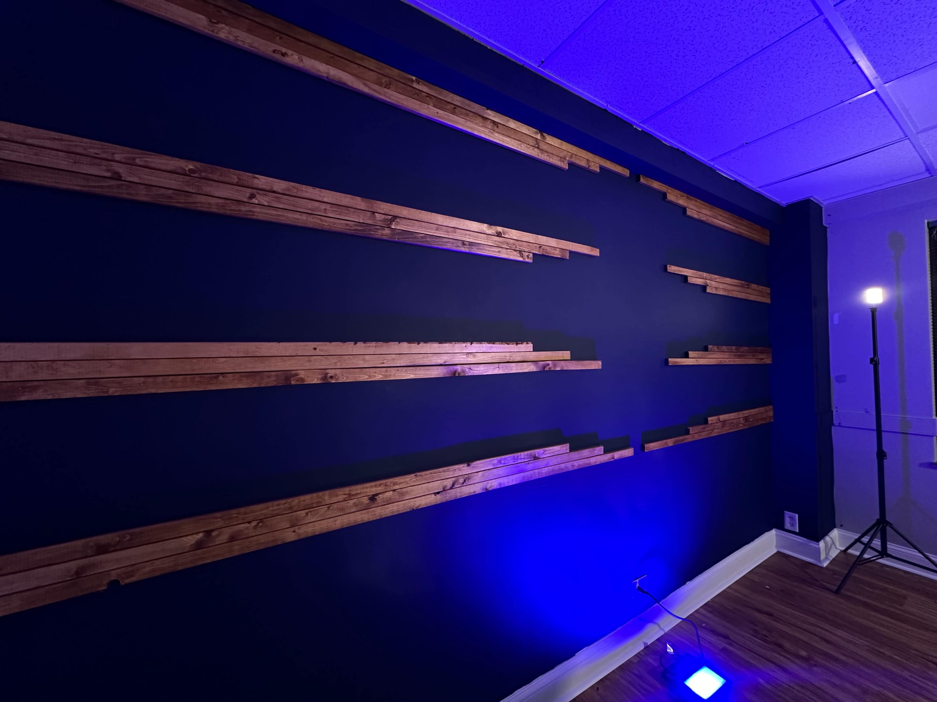 The image shows a dark blue wall with wooden strips arranged horizontally and a spot light illuminating the corner.