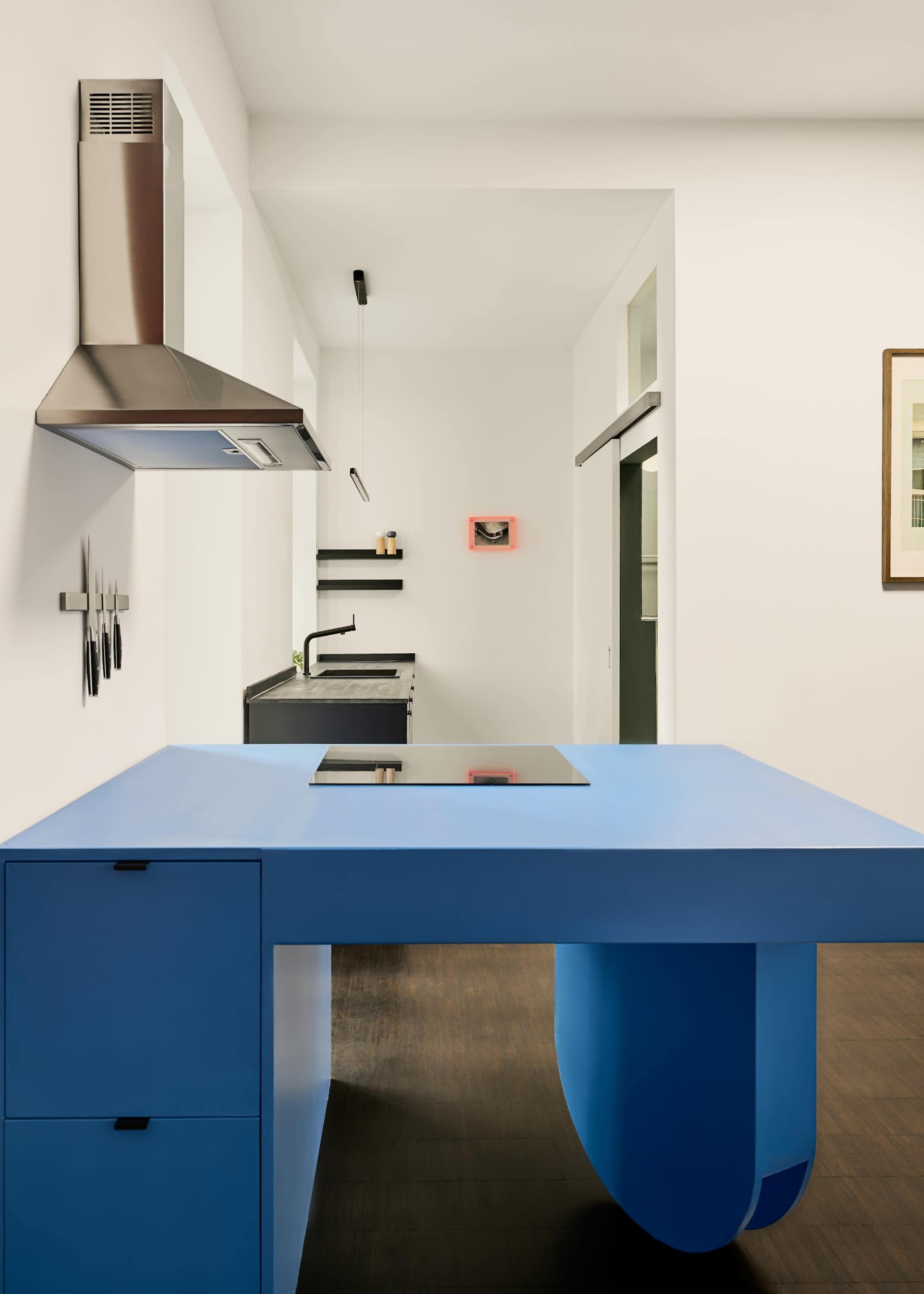 The image shows a modern kitchen featuring a blue island with drawers, stainless steel appliances, and minimalistic decor on the walls.