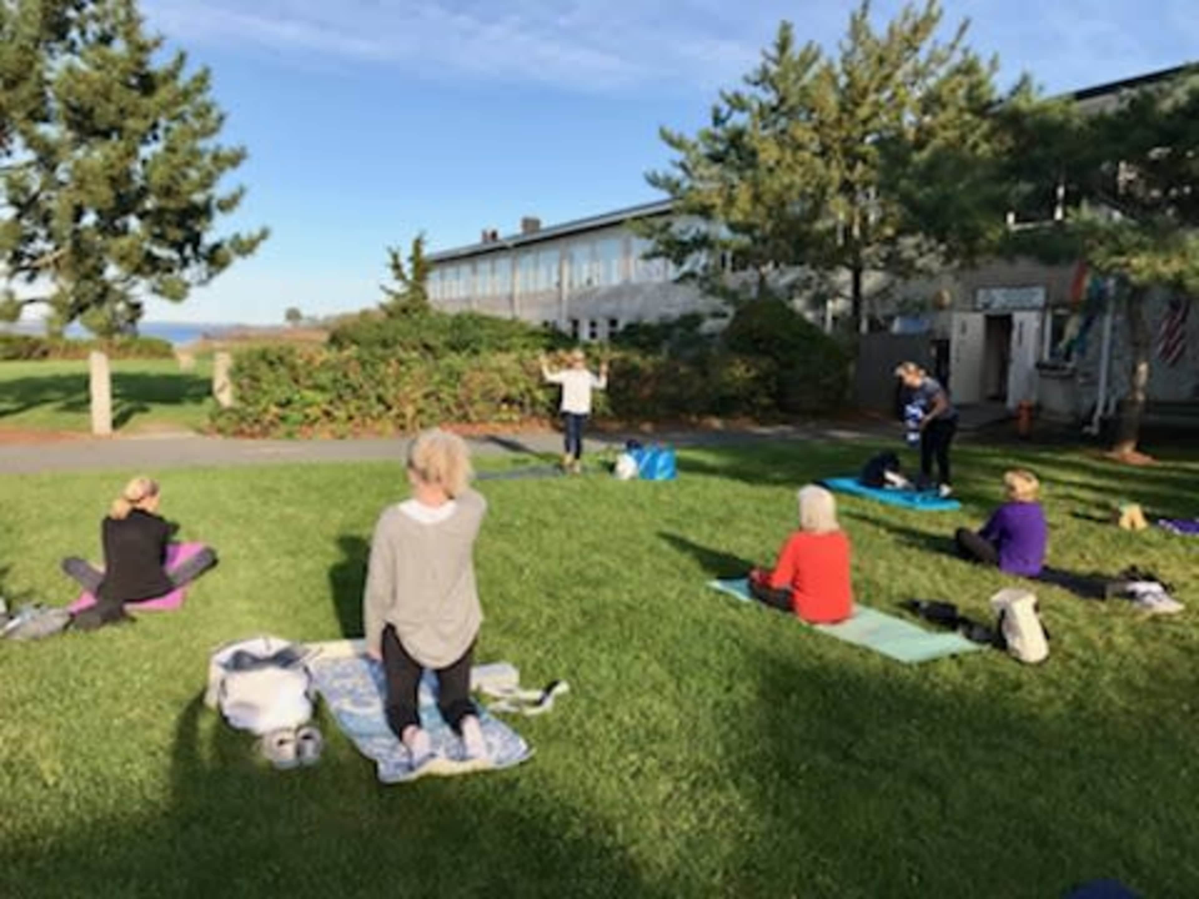 A group of people is practicing yoga on mats in a grassy area near a building on a clear day.