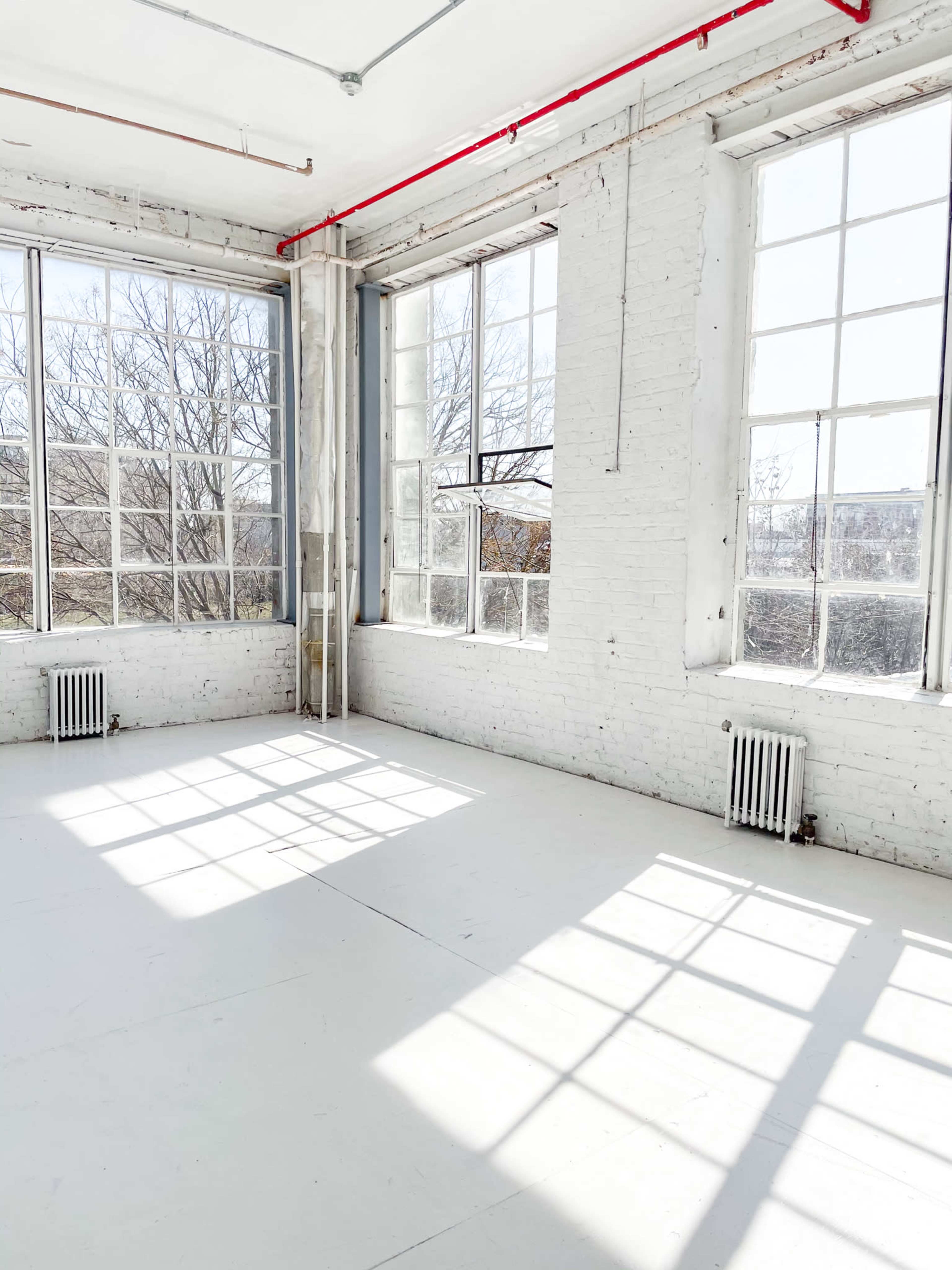 A bright, empty room with large windows that cast shadows on the white floor.