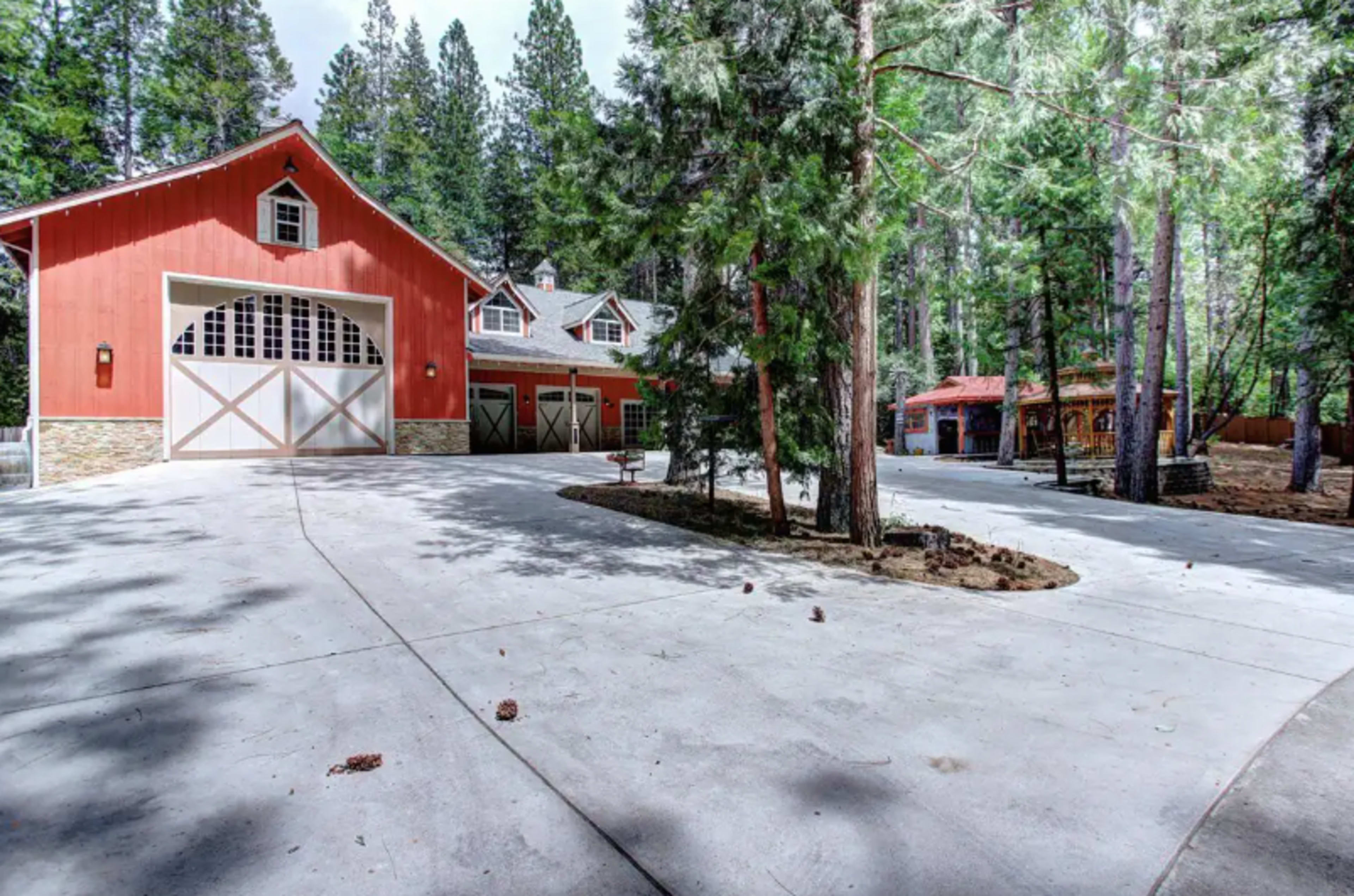 A red barn-style building with a large driveway surrounded by tall trees in a forested area.