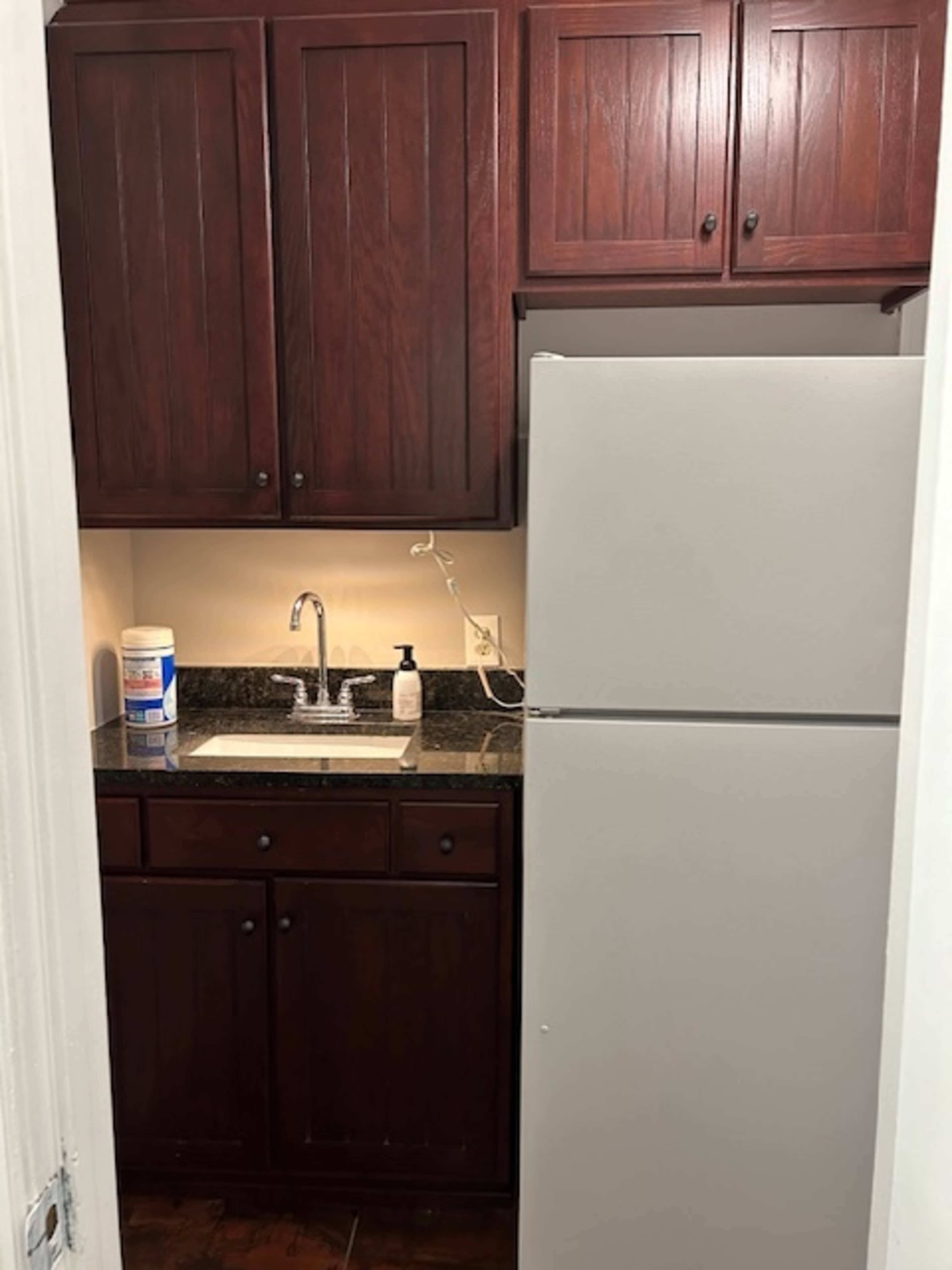 A small kitchen area with dark wood cabinets, a white refrigerator, and a sink with a granite countertop.