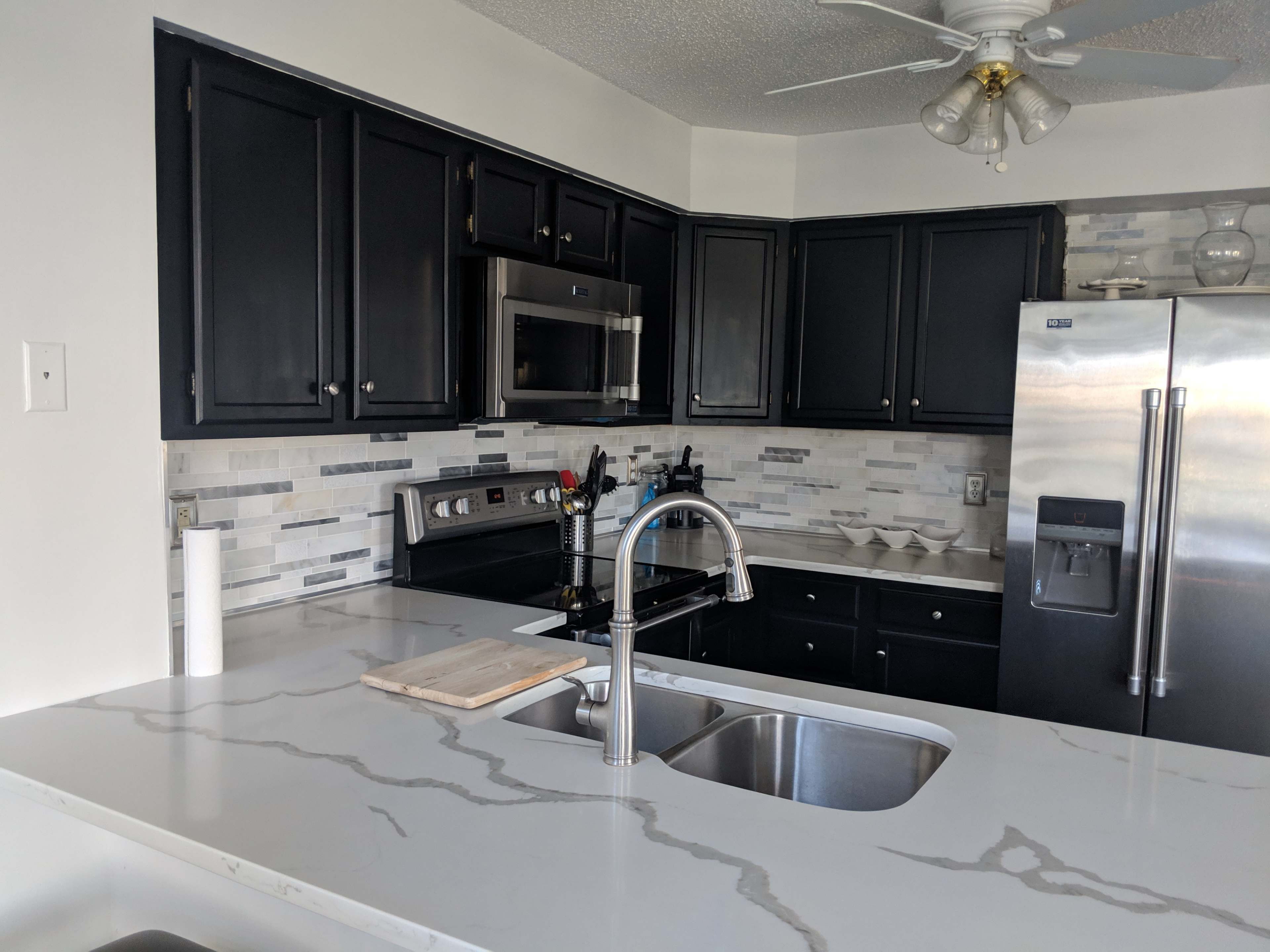 A kitchen with dark cabinets, stainless steel appliances, and a marble countertop featuring a double sink.